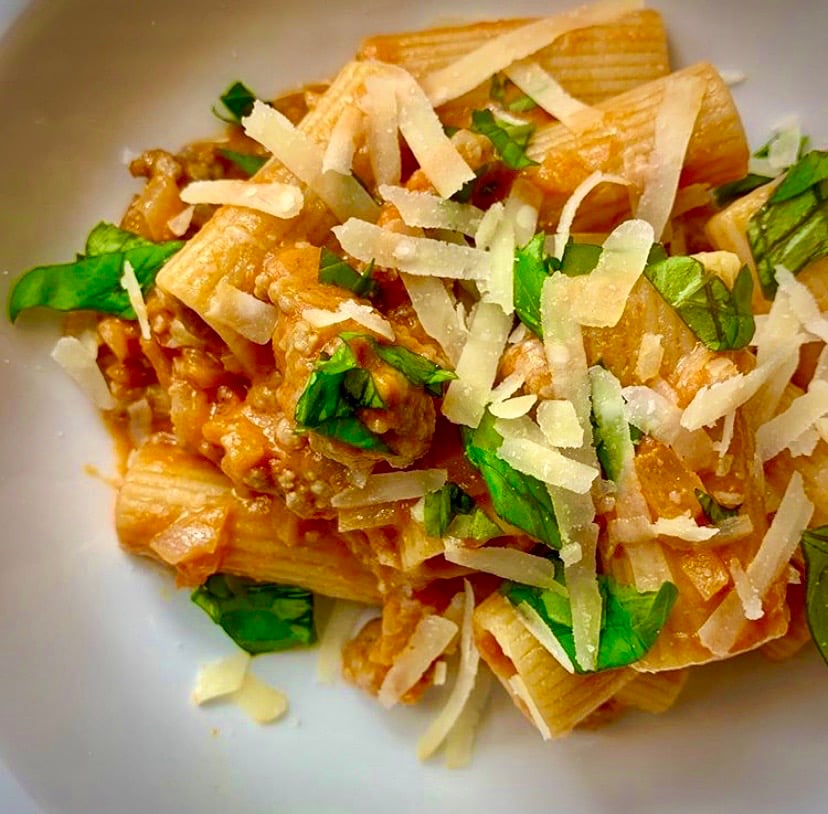 Italian sausage pasta on a white plate garnished with parmesan and basil