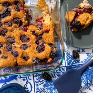 blackberry cobbler in a baking dish with a slice on a plate.