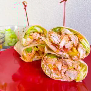 buffalo chicken wraps cut in half on red plate with bowl of lettuce in the background.