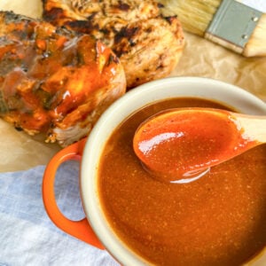 BBQ sauce in a bowl with a spoon and grilled chicken in the background