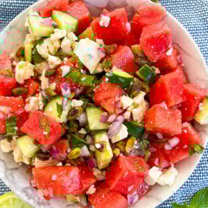 Watermelon feta salad in a white bowl with squeezed limes and mint around it