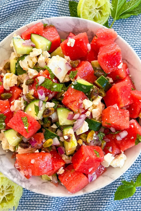 Watermelon feta salad in a white bowl with squeezed limes and mint around it