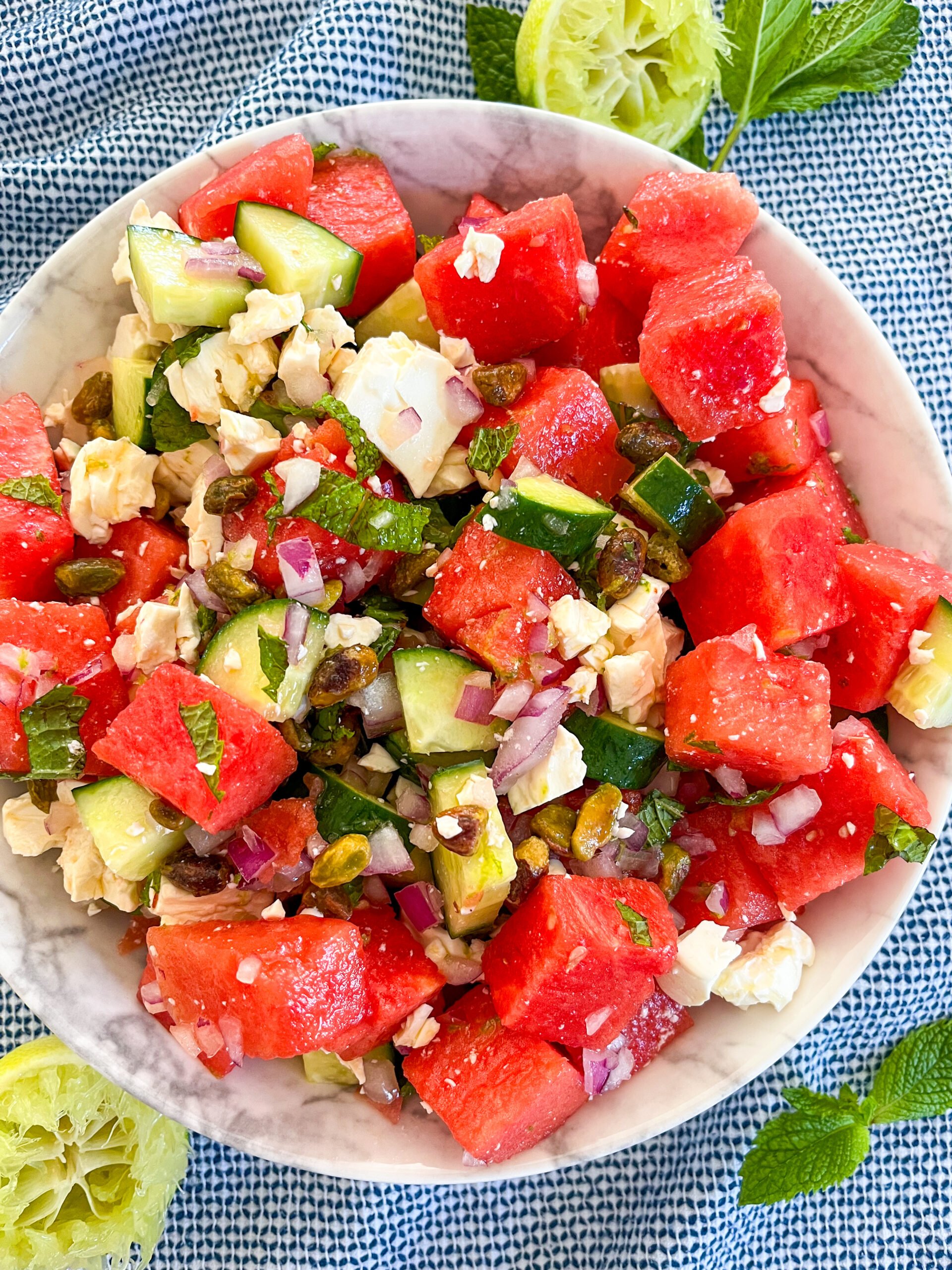 Watermelon feta salad in a white bowl with squeezed limes and mint around it