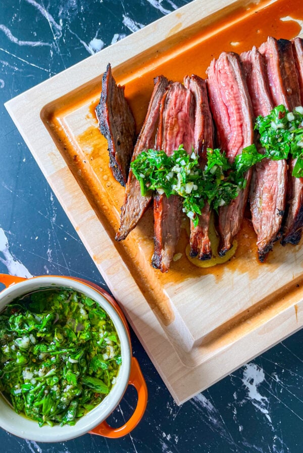Chimichurri in a small bowl next to a sliced grilled steak on a cutting board