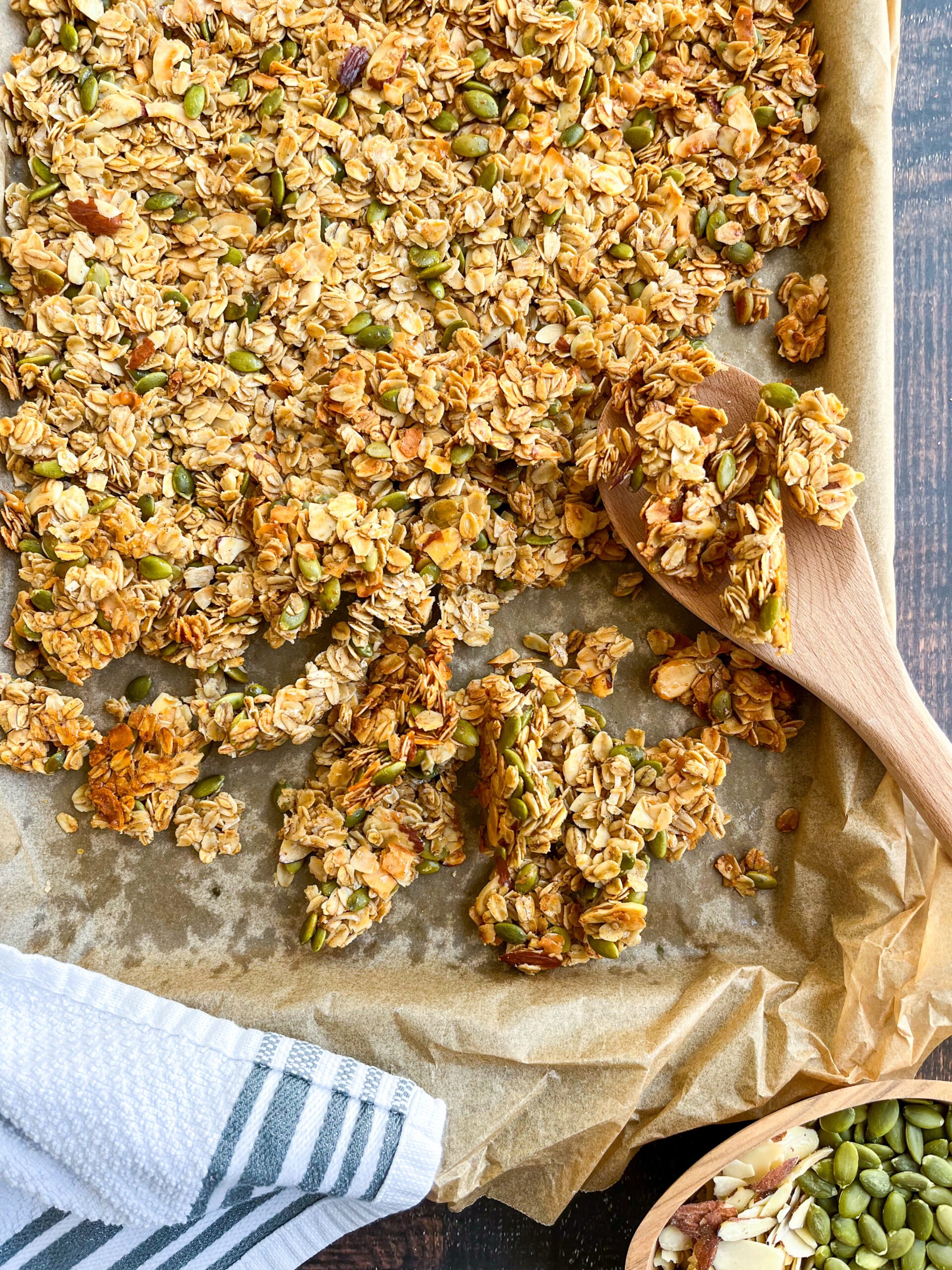 Homemade granola on a baking sheet with a wooden spoon