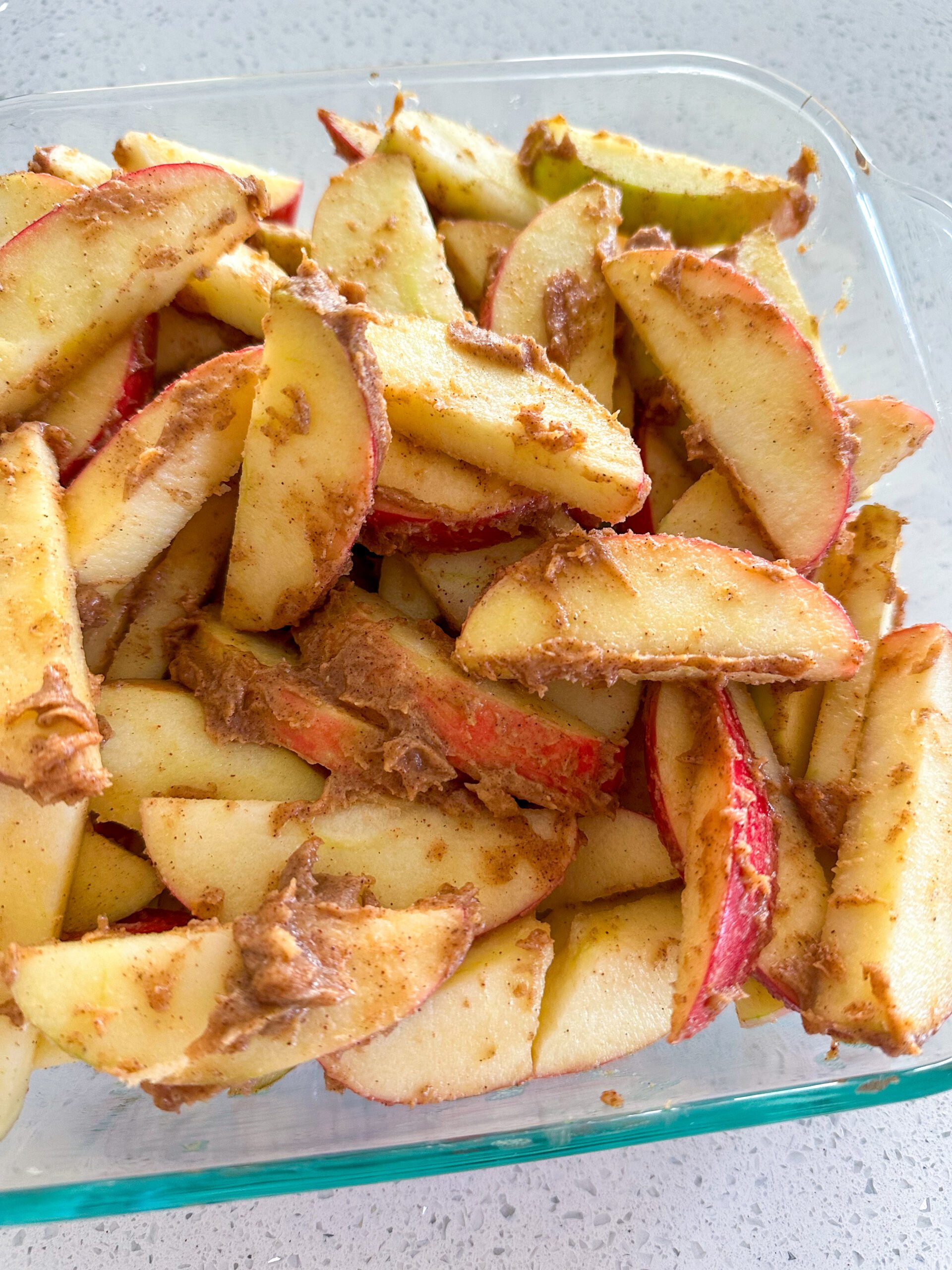 Apples tossed in cinnamon mixture spread out in glass pan