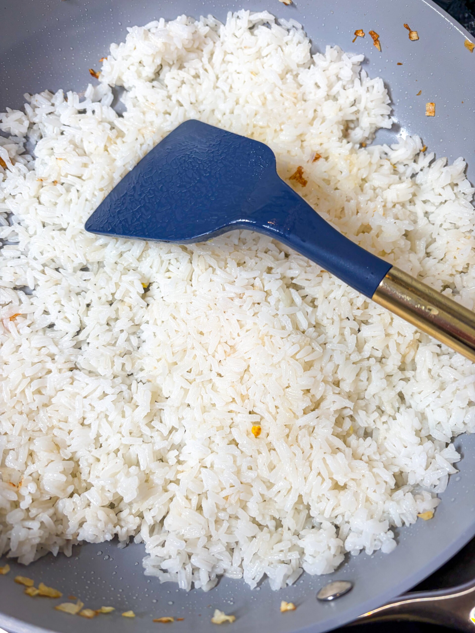 Frying rice in a large pan with blue spatula