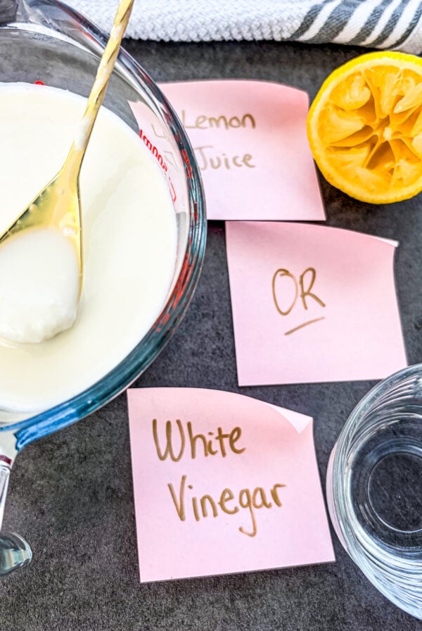 Homemade buttermilk being stirred next to white vinegar and a lemon halve