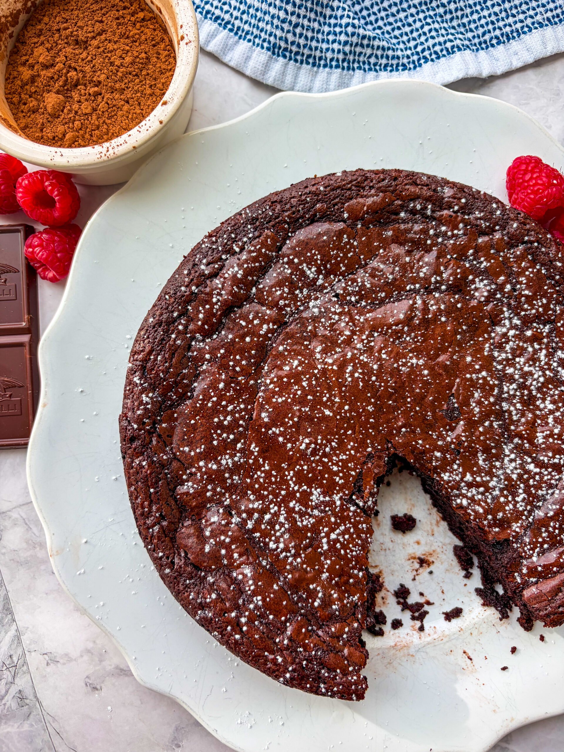 One slice taken out of chocolate flourless cake on a white plate