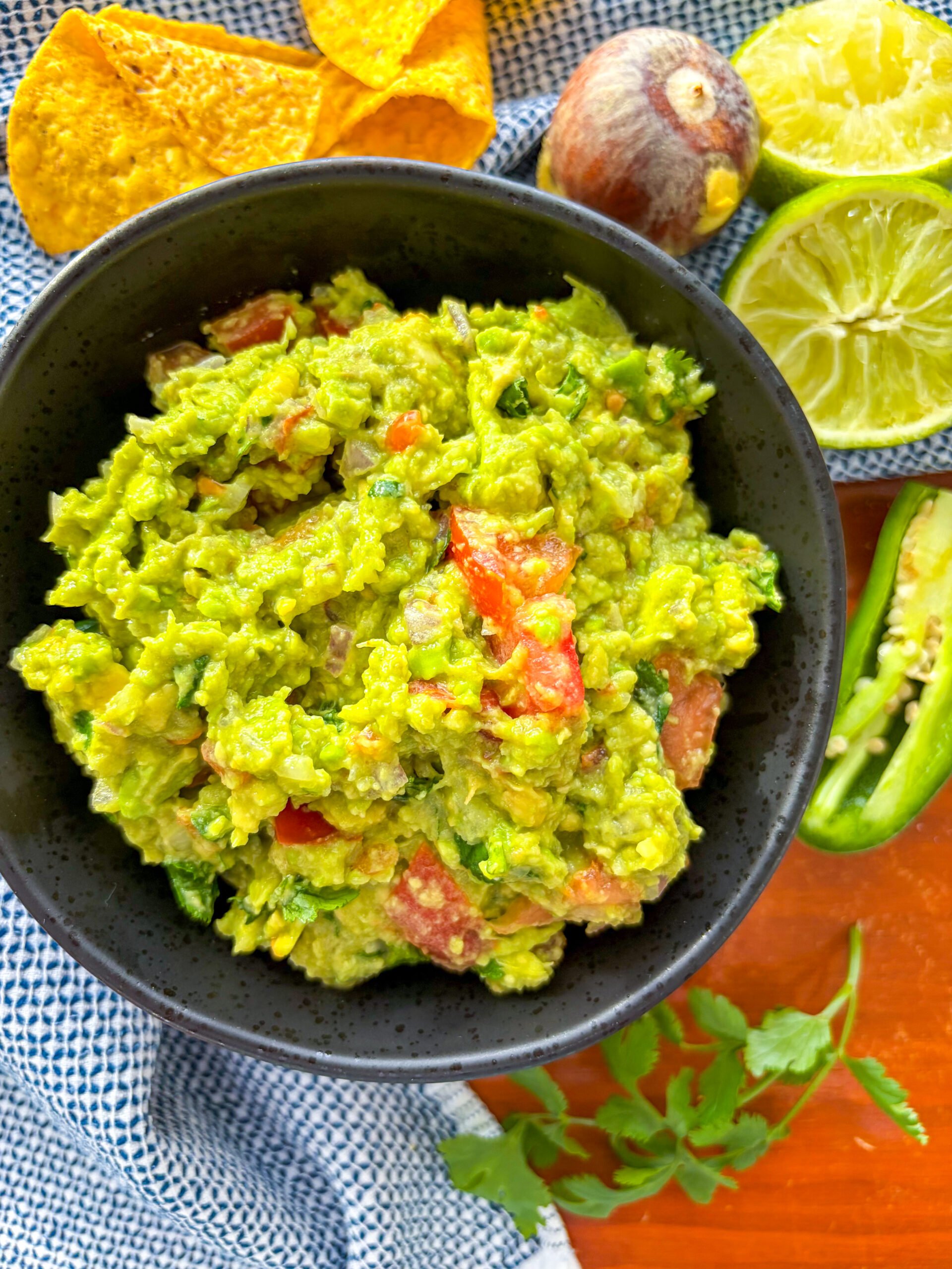 Guacamole in a black bowl with chips, lime and jalape&ntilde;o on side