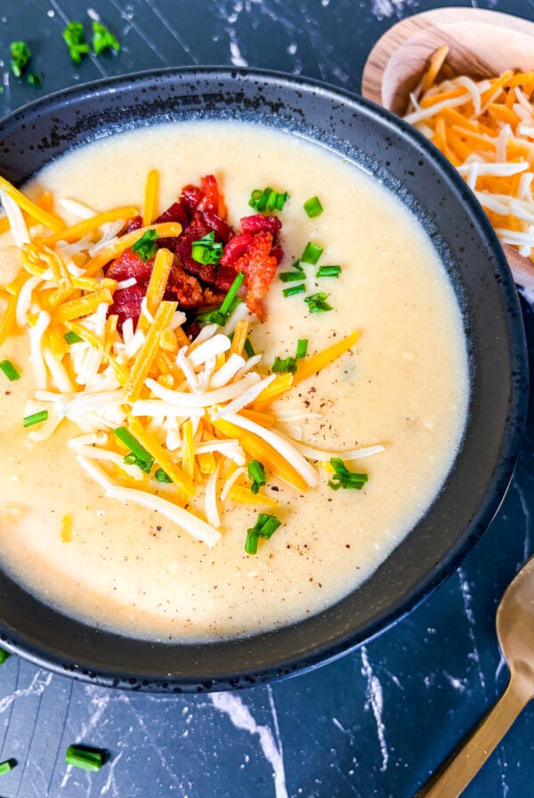 Close up of potato soup in a black bowl topped with cheese, bacon and chive
