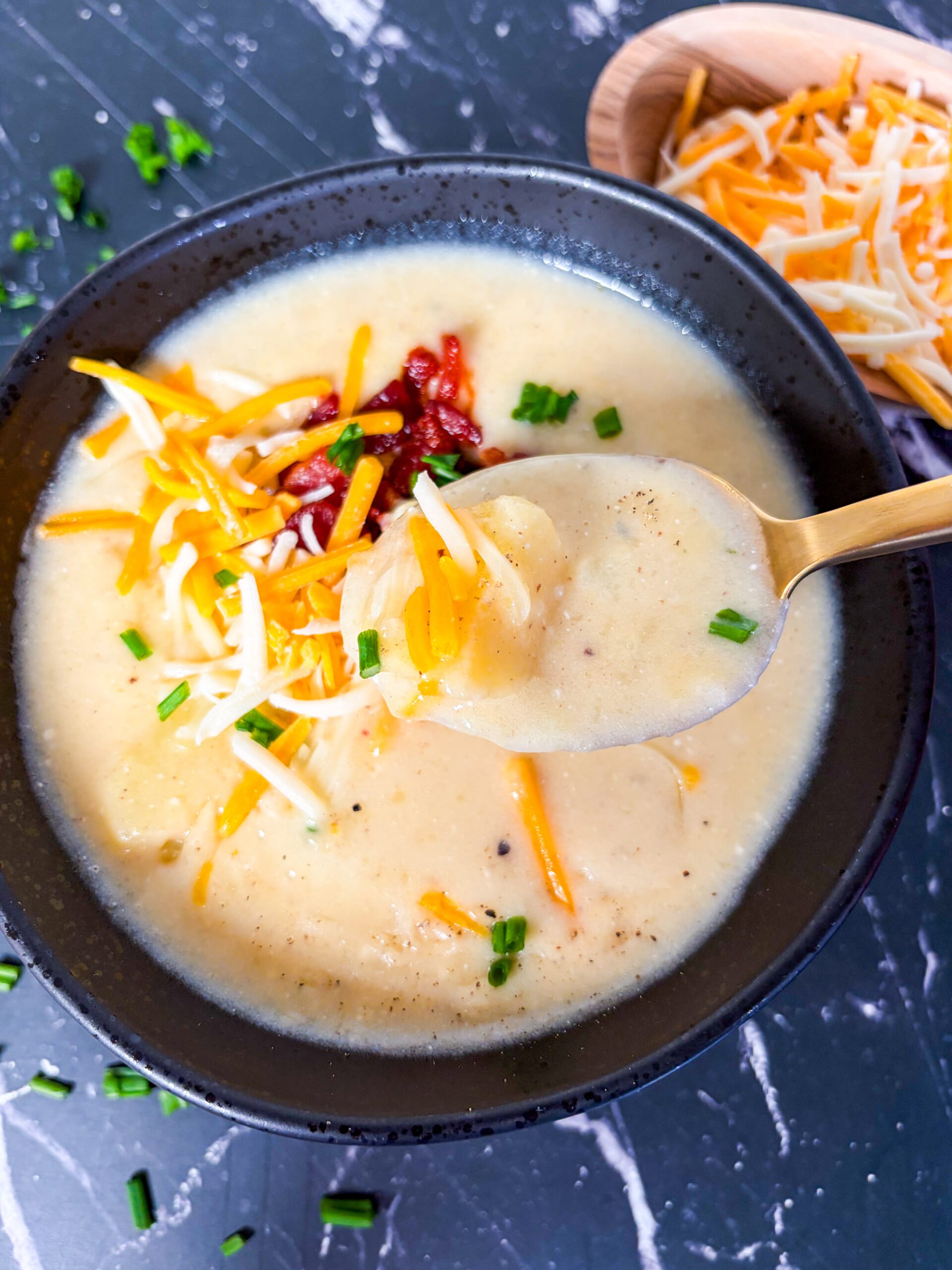 Close up of potato soup in a black bowl scooped with a spoon