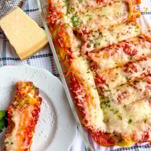 Manicotti in a baking dish and one on a plate next to parm block