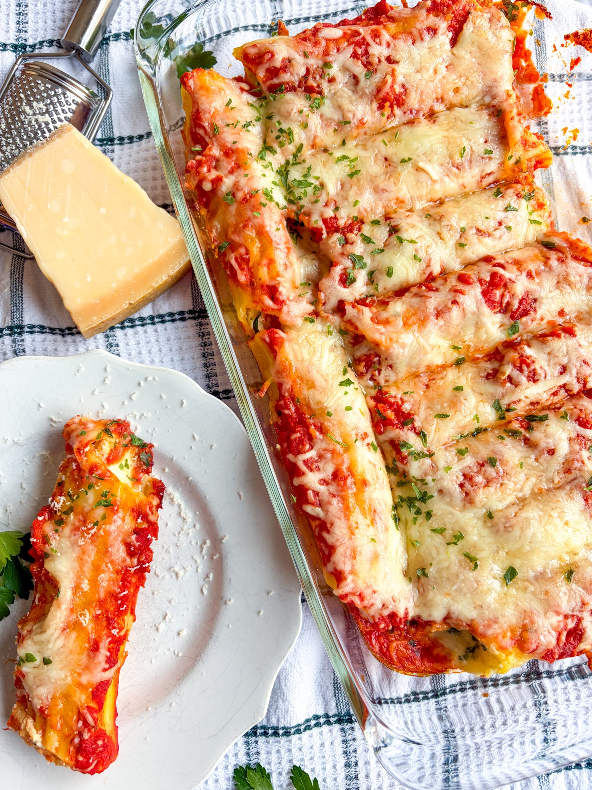 Manicotti in a baking dish and one on a plate next to parm block