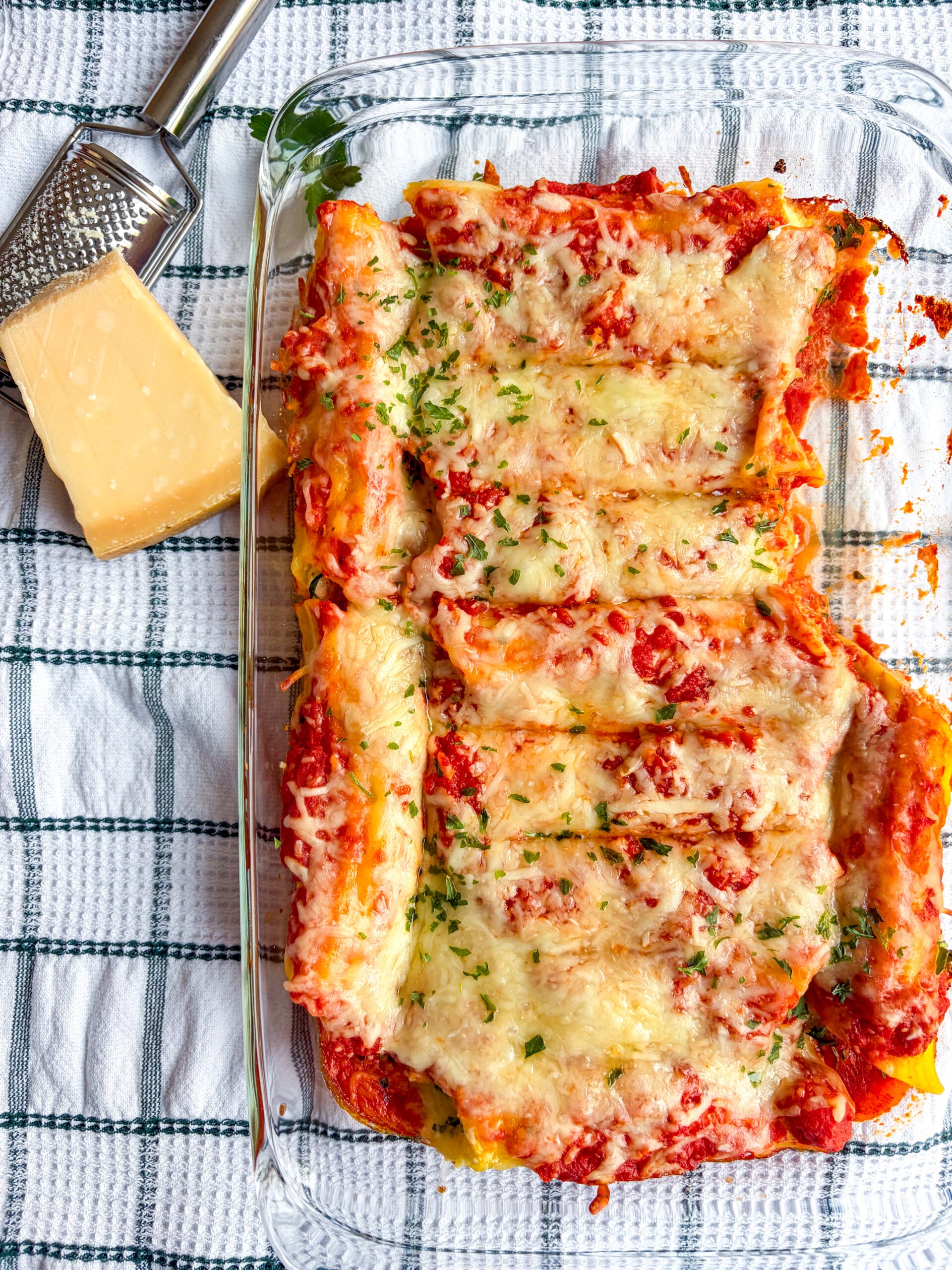 Manicotti in baking fish next to parm block with grater