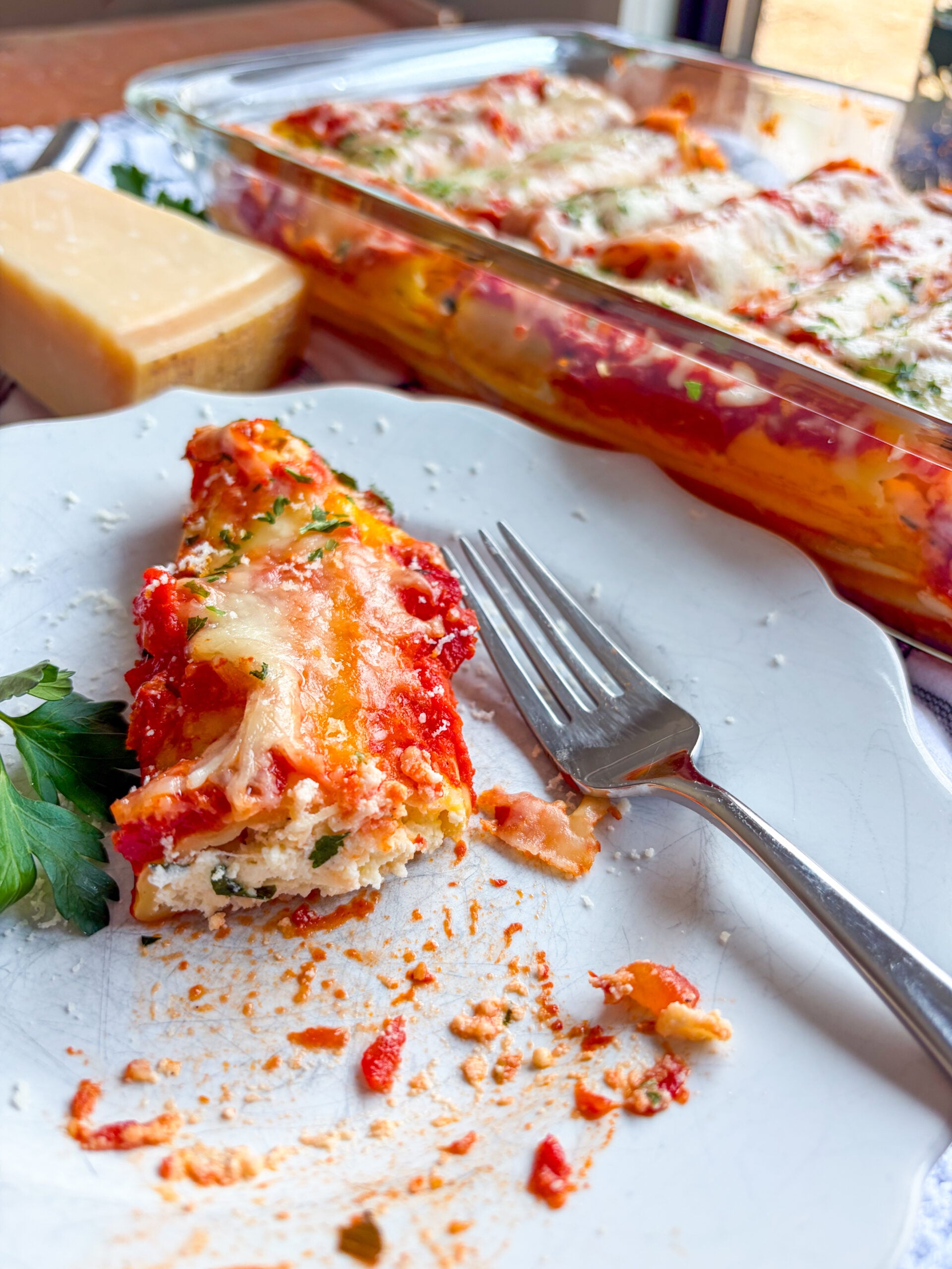 Manicotti cut open on a plate with fork and baking dish in background