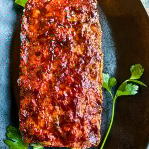 Close up of meatloaf on black plate garnished with parsley