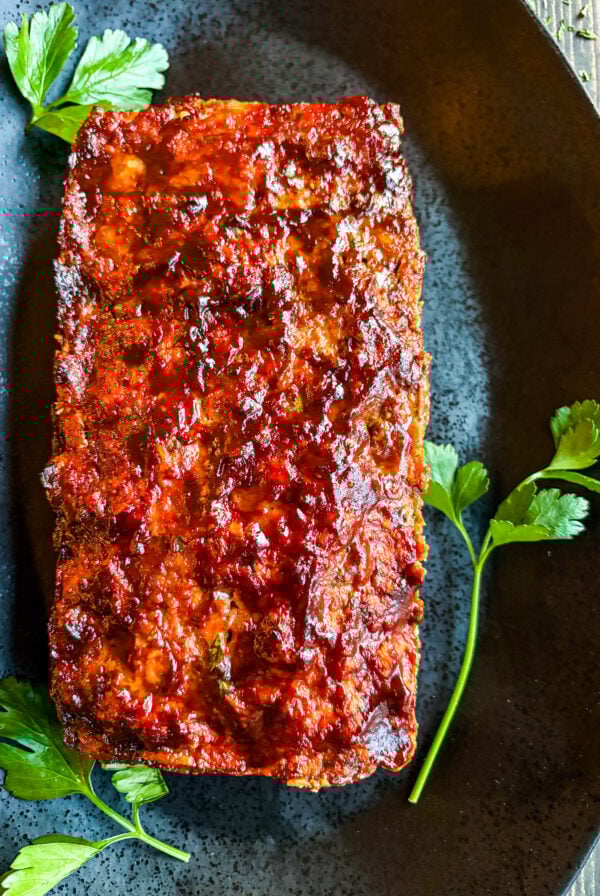 Close up of meatloaf on black plate garnished with parsley