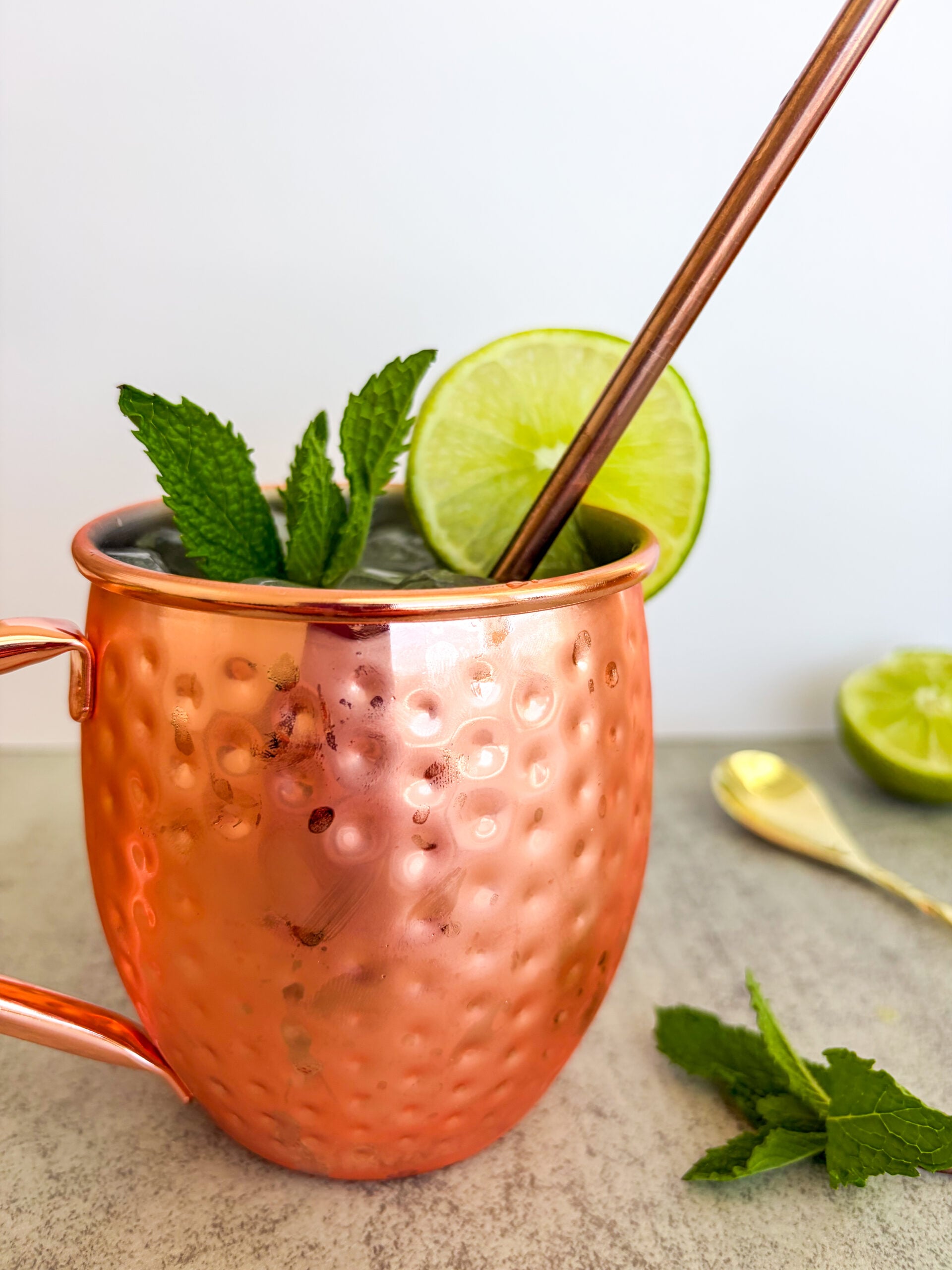 Closer up of Moscow mule in a copper cup with straw and garnished with lime and mint
