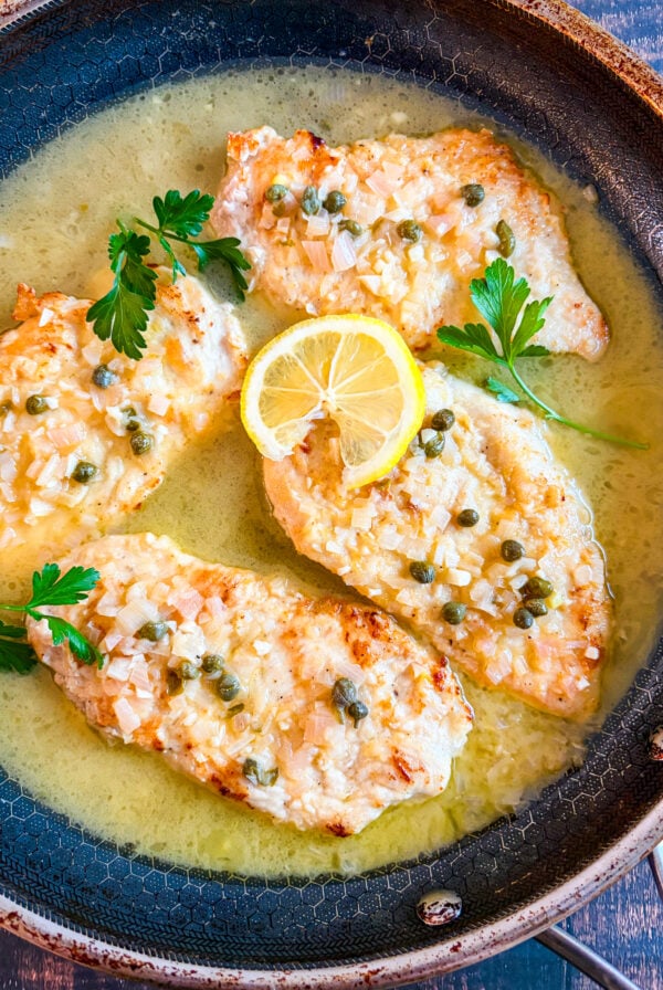 Chicken piccata in a pan garnished with parsley and lemon wheel
