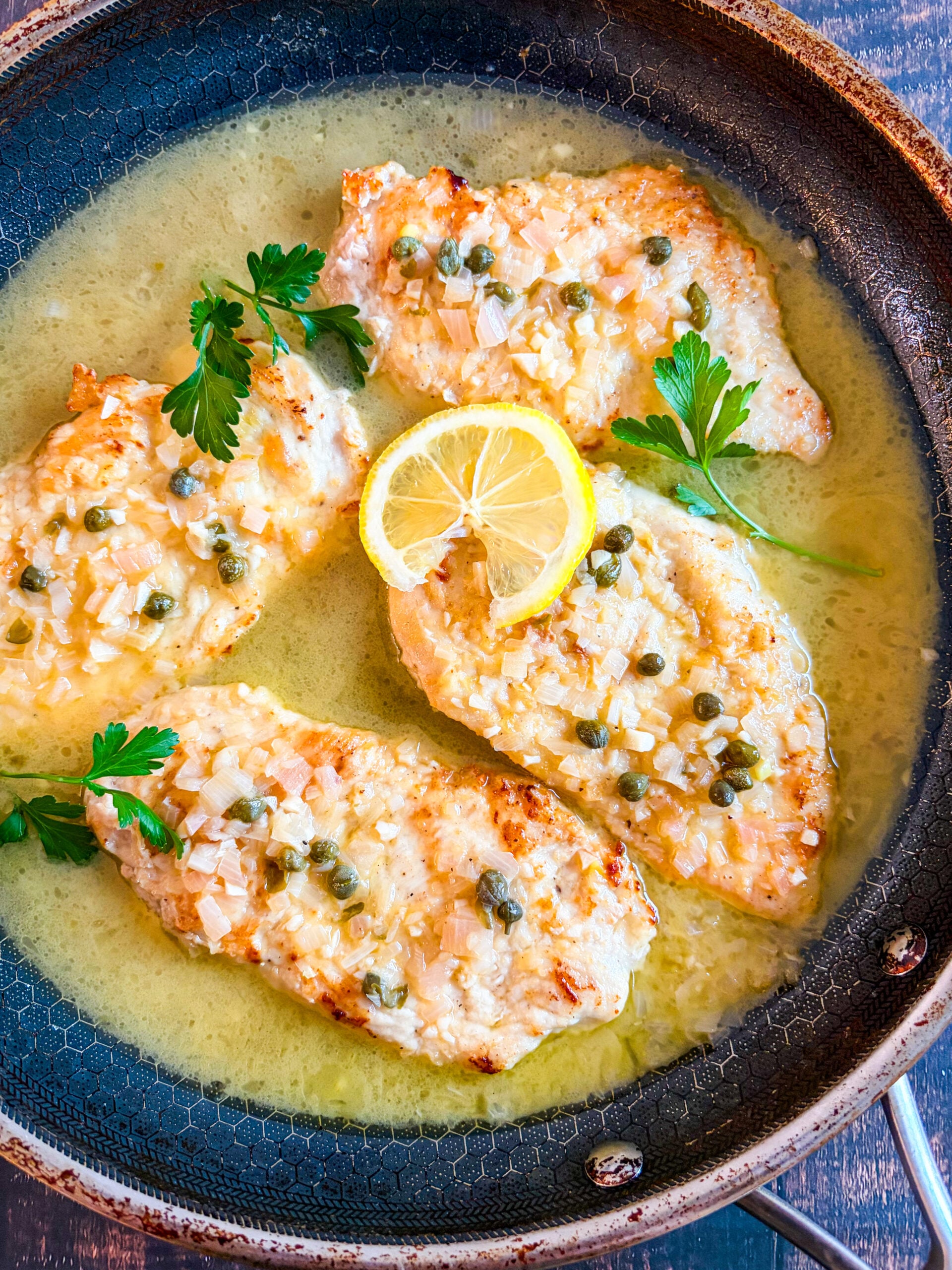 Chicken piccata in a pan garnished with parsley and lemon wheel