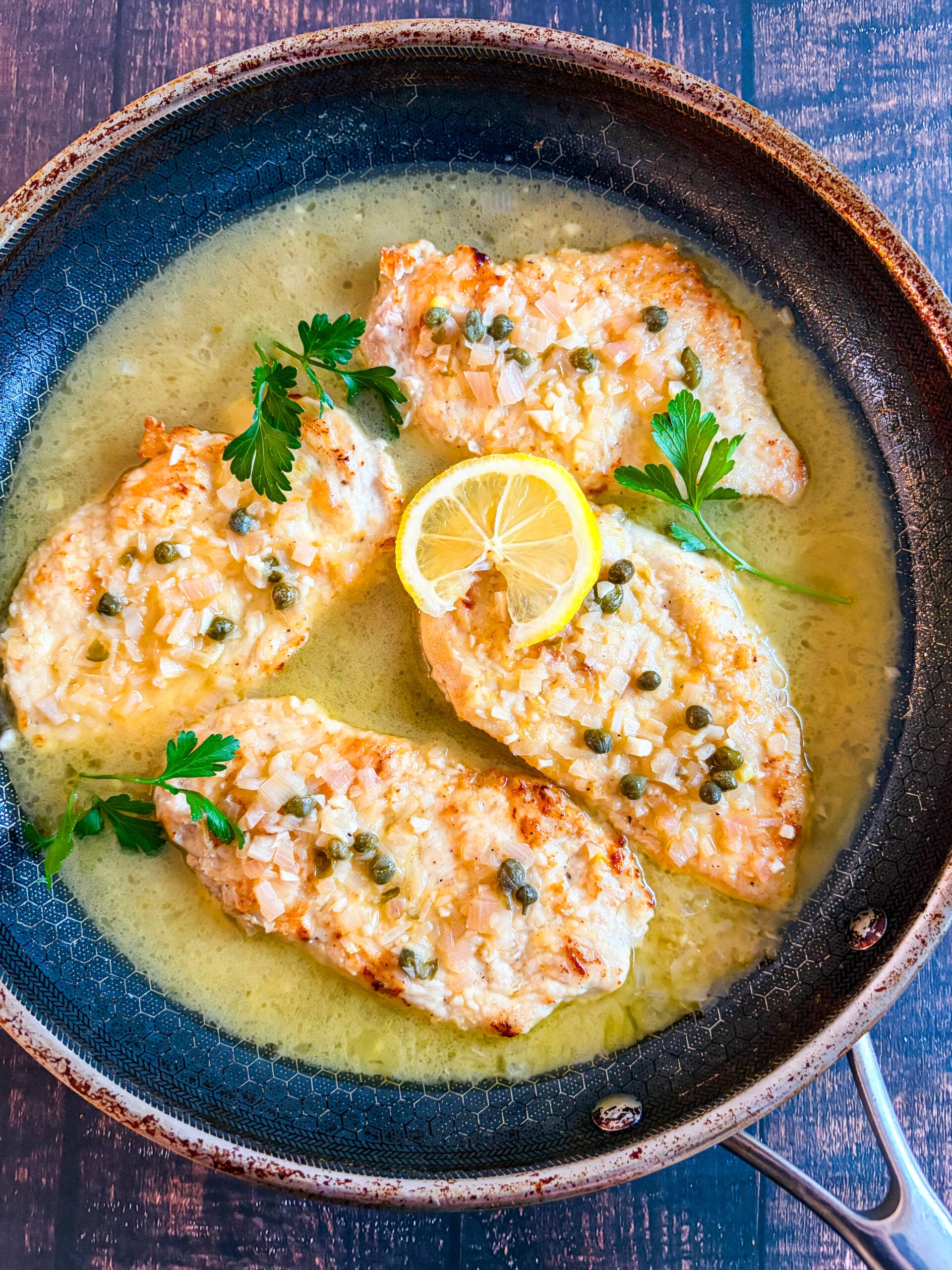 Further away shot of chicken piccata in pan with lemon and parsley