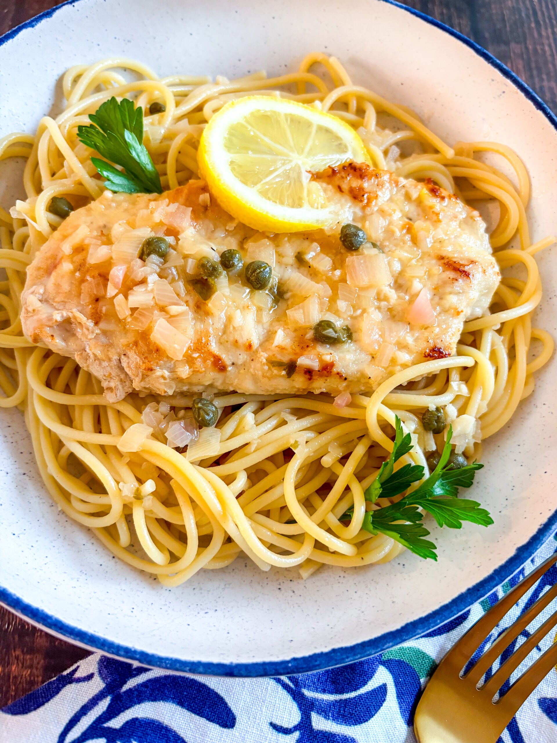 Chicken piccata in a blue and white bowl over spaghetti