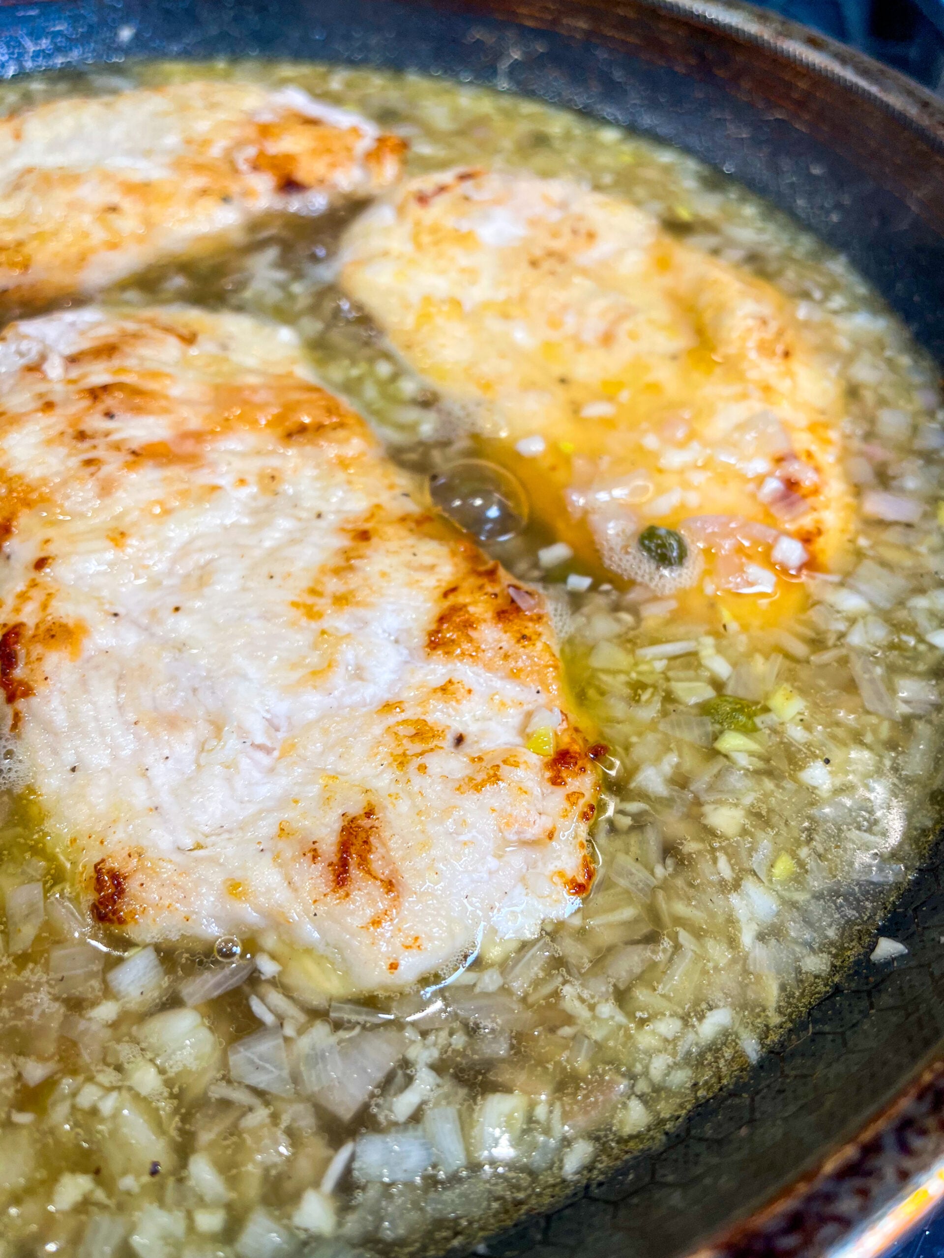 Pan seared chicken in pan simmering with piccata sauce
