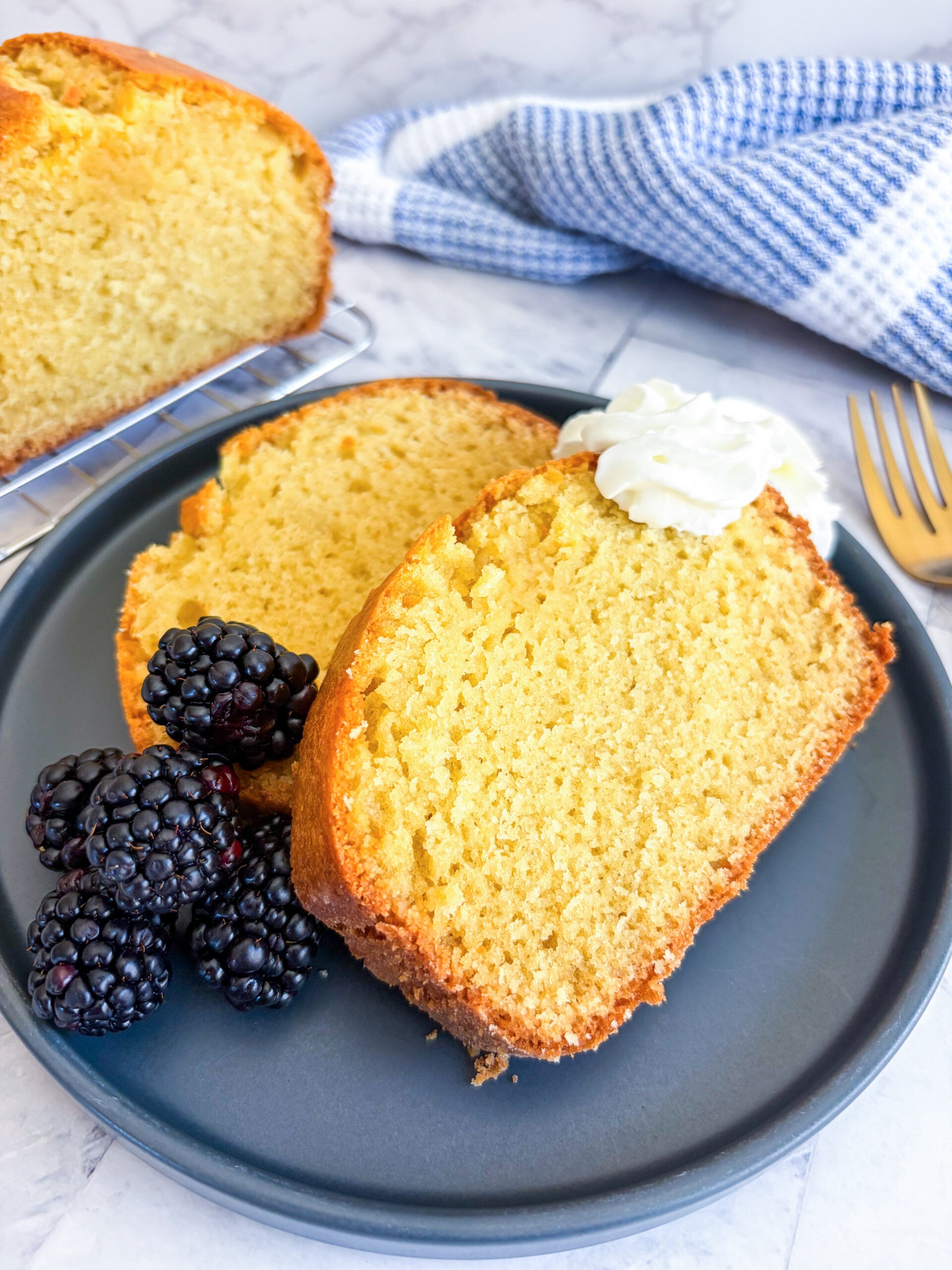 Slices of pound cake on a plate with blackberries and whipped cream