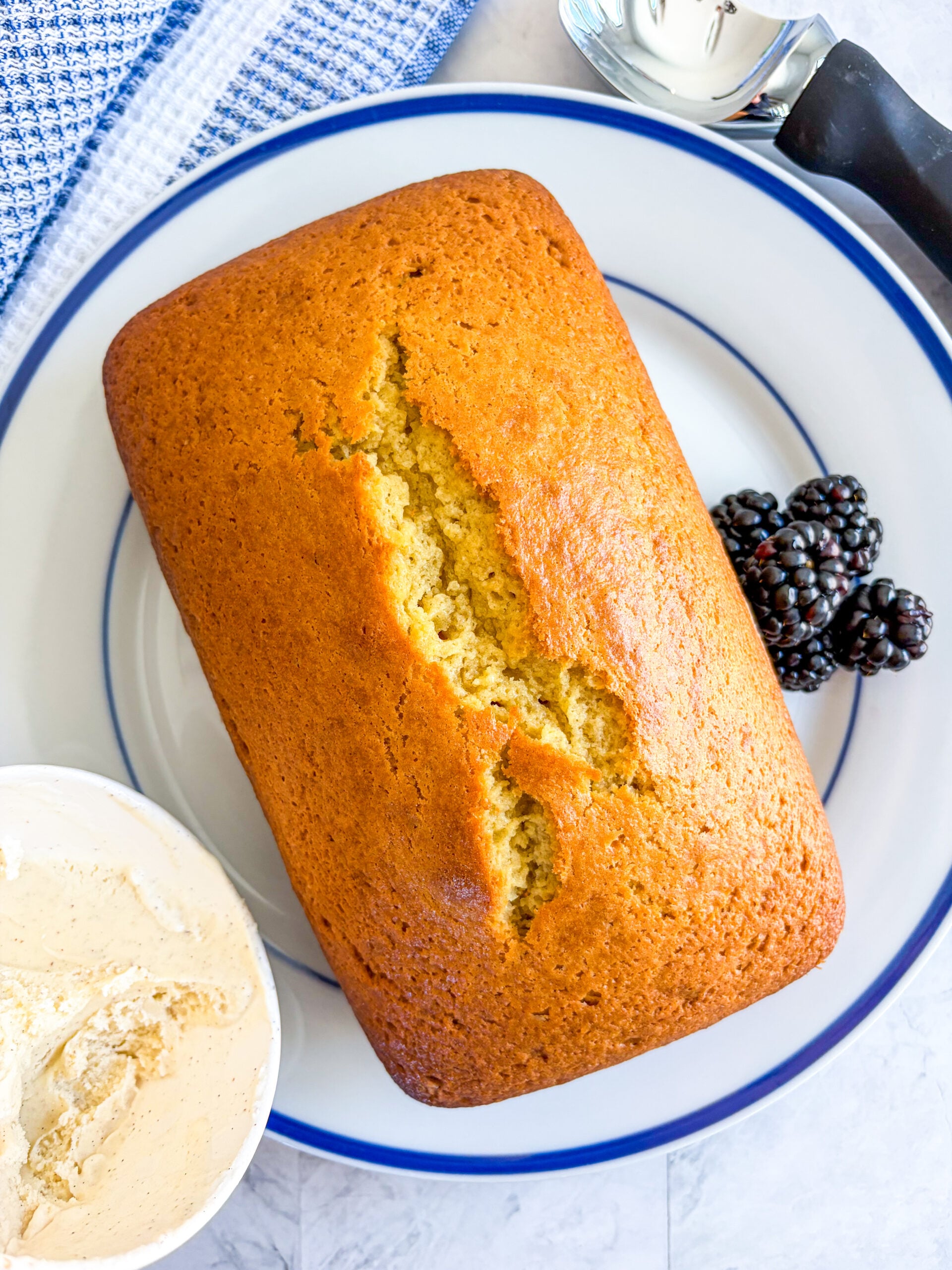Pound cake on a blue and white plate with berries and vanilla ice cream on side
