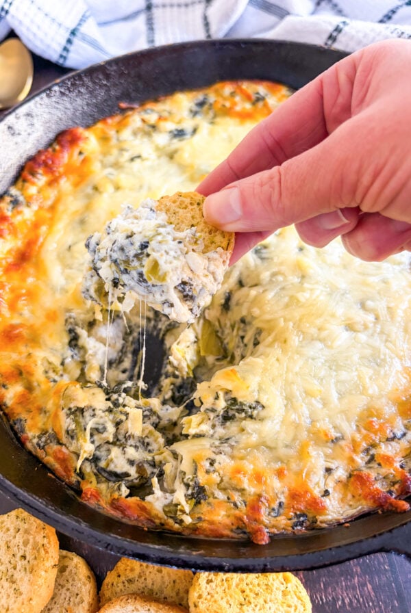 Scooping up dip with crostini in a skillet
