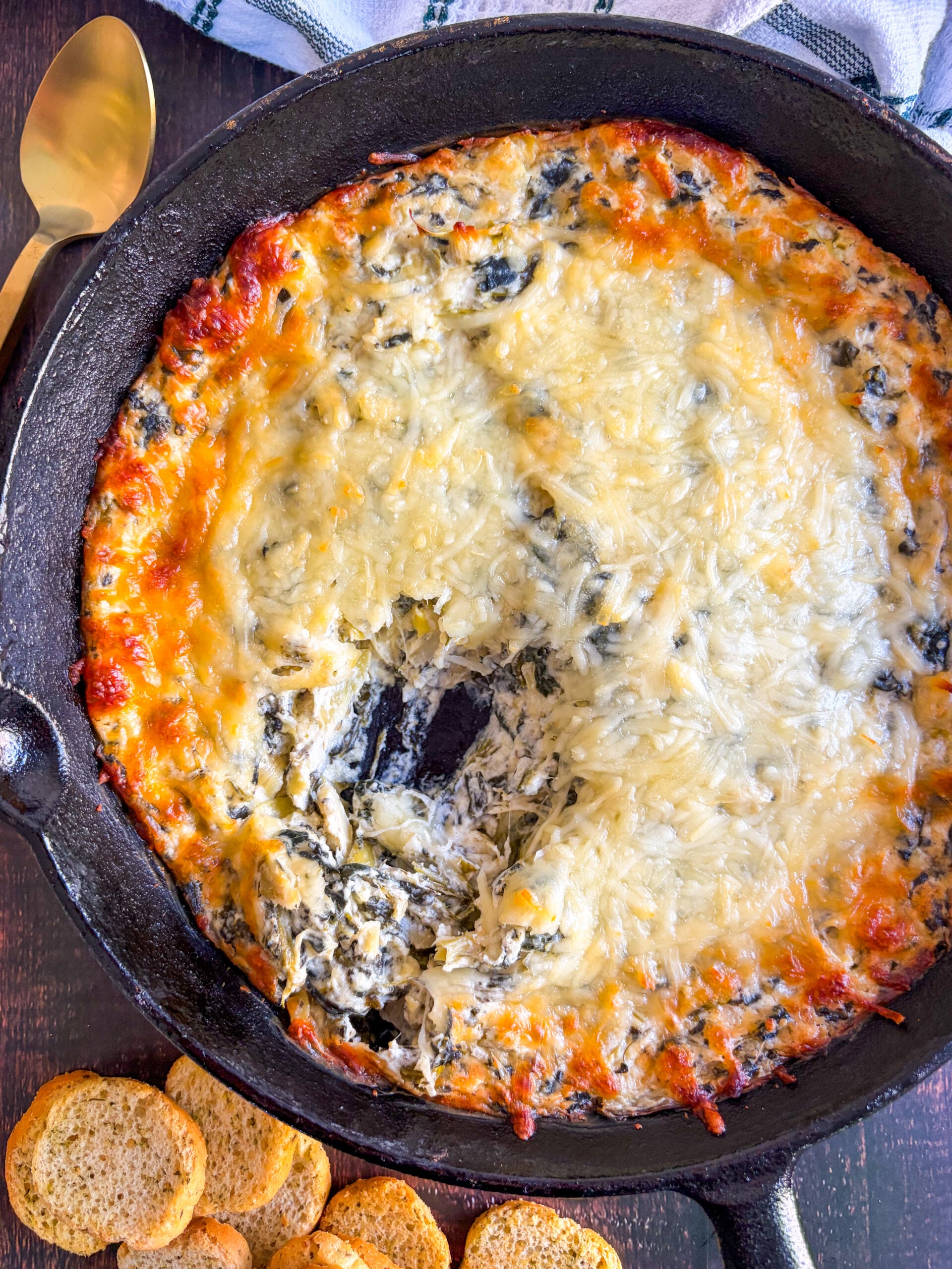 Spinach artichoke dip in black skillet next to crostini