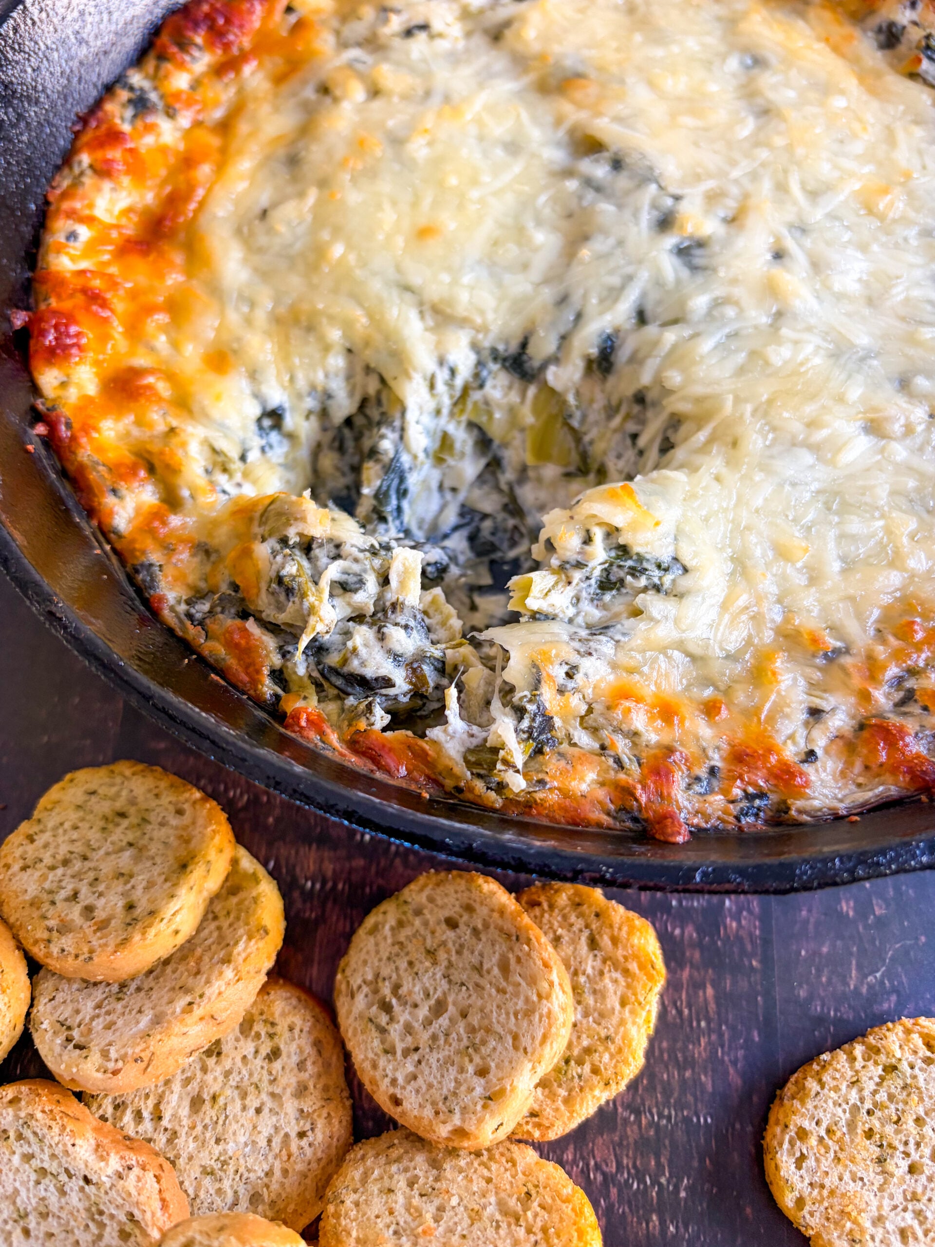 Close up of spinach artichoke dip in black skillet next to crostini