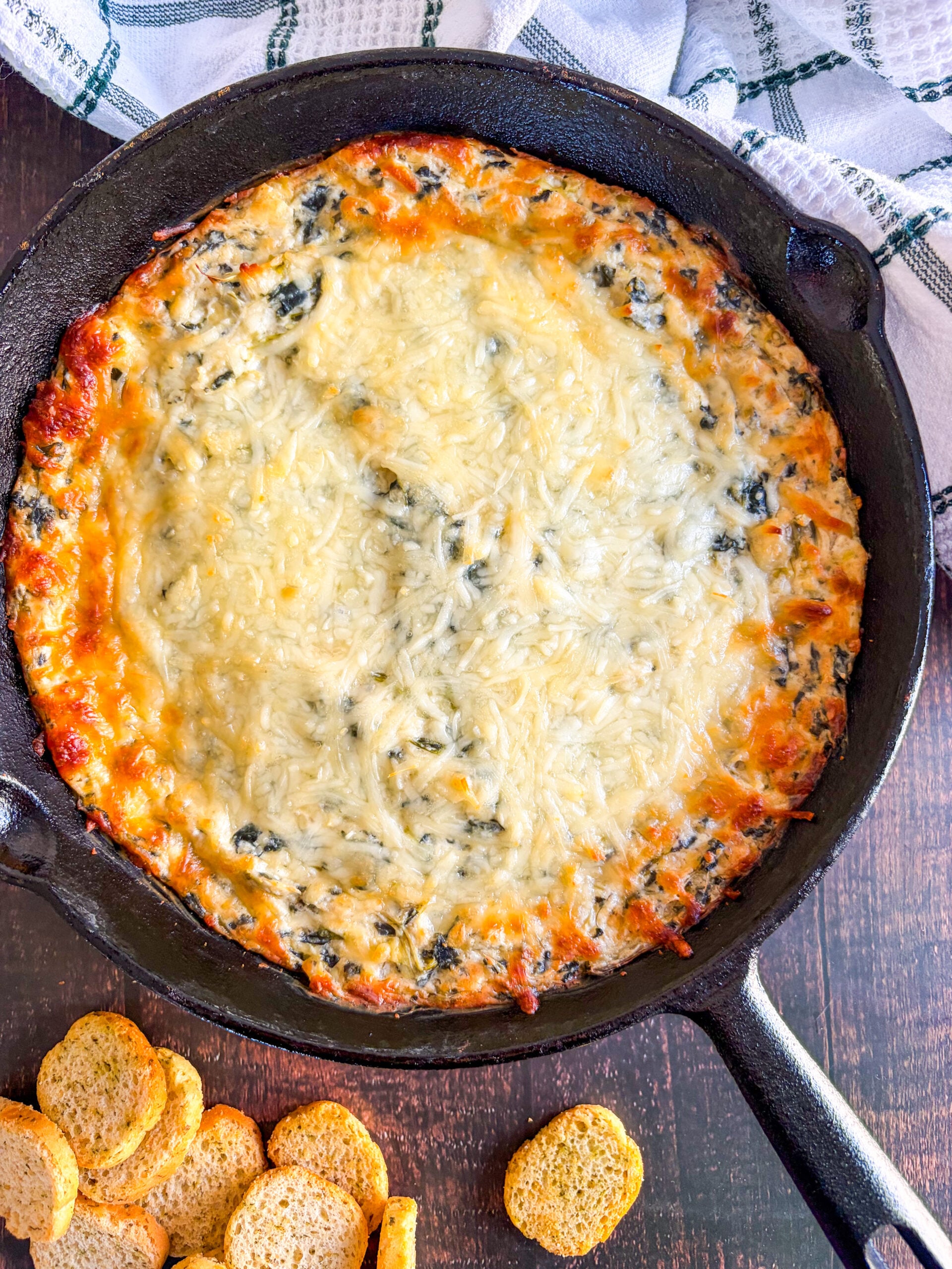 Just baked spinach artichoke dip in black skillet next to crostini