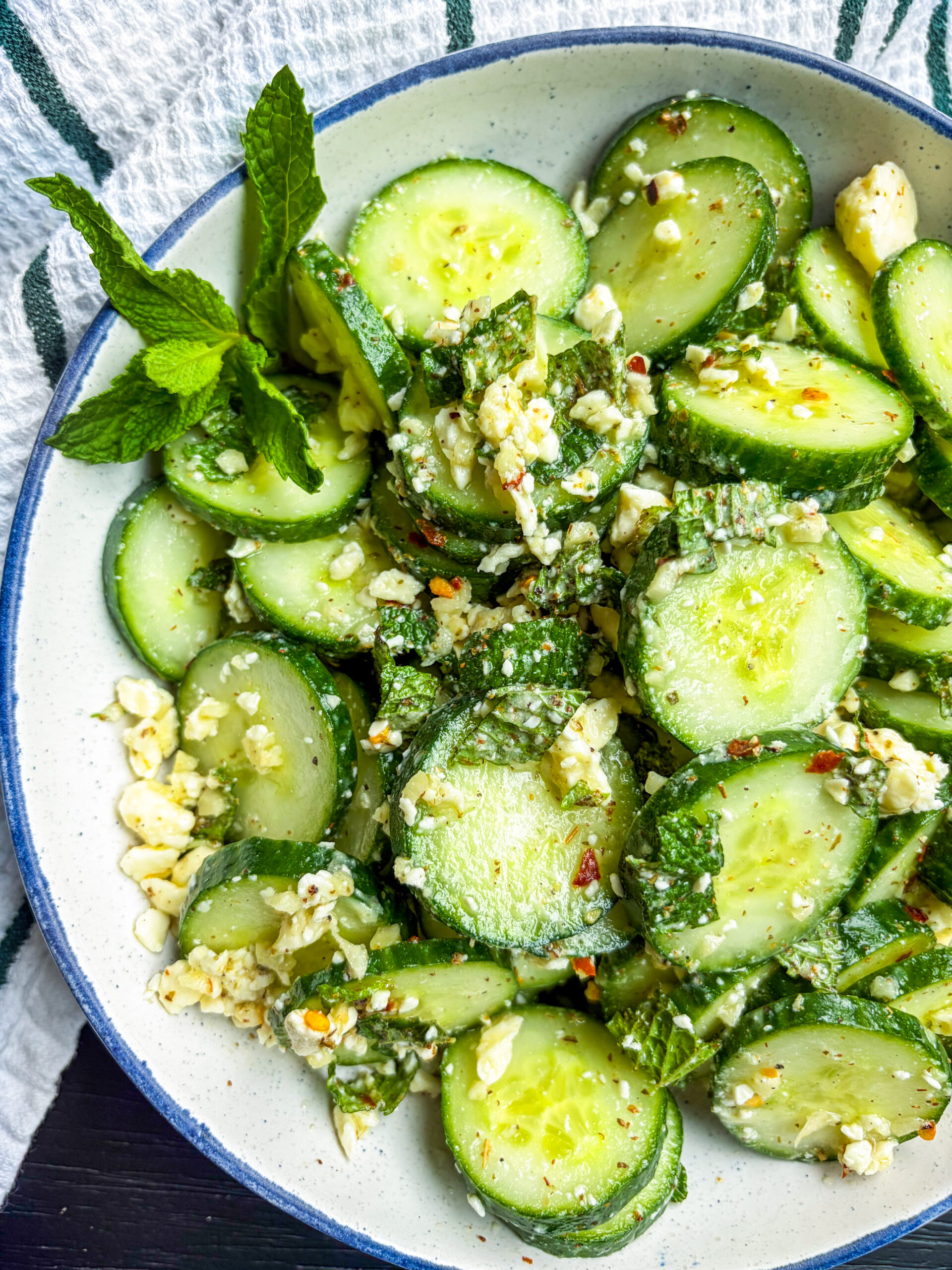 Cucumber salad in a blue and white bowl garnished with mint