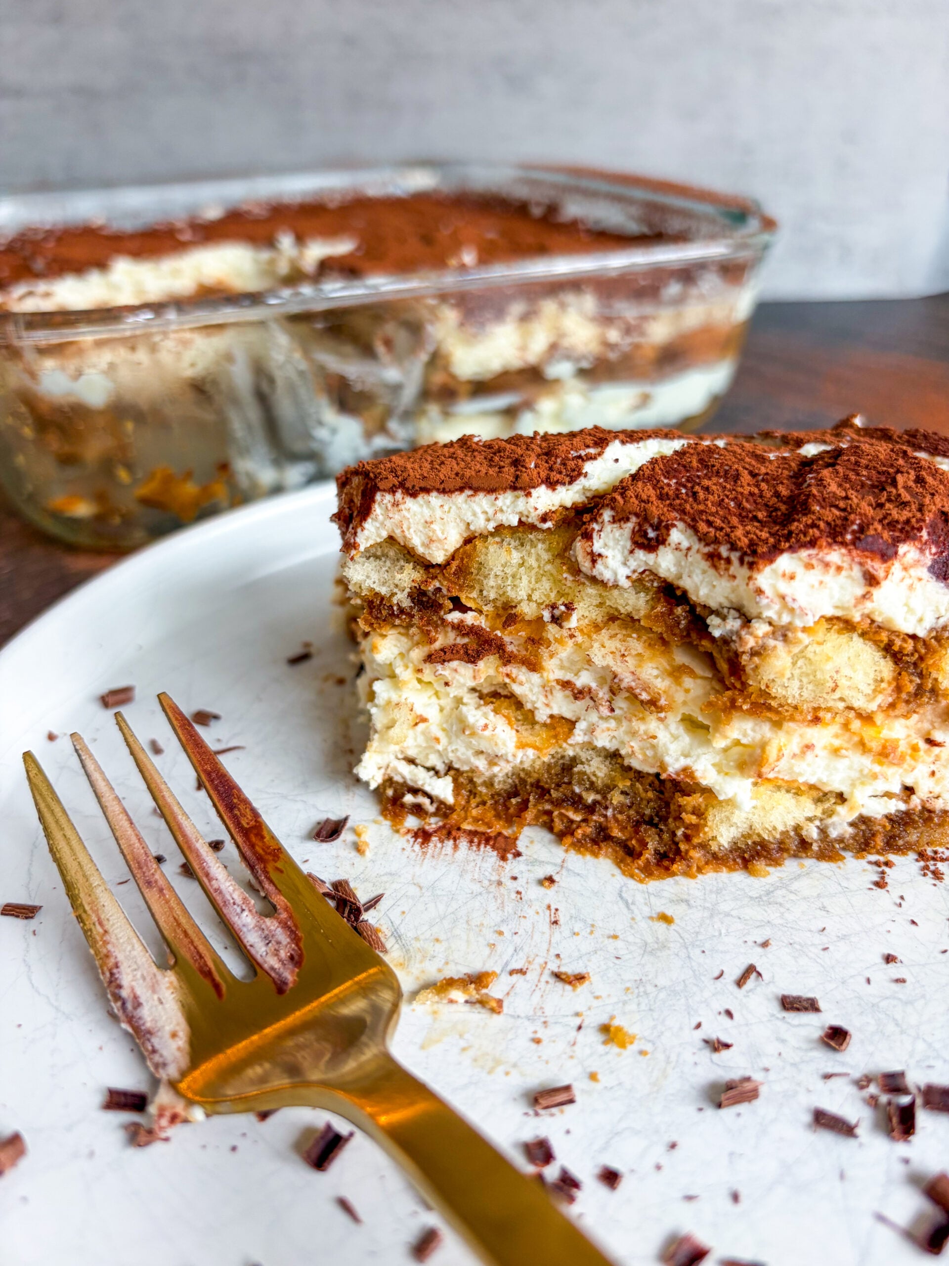 Tiramisu slice on white plate with gold fork, bite taken out