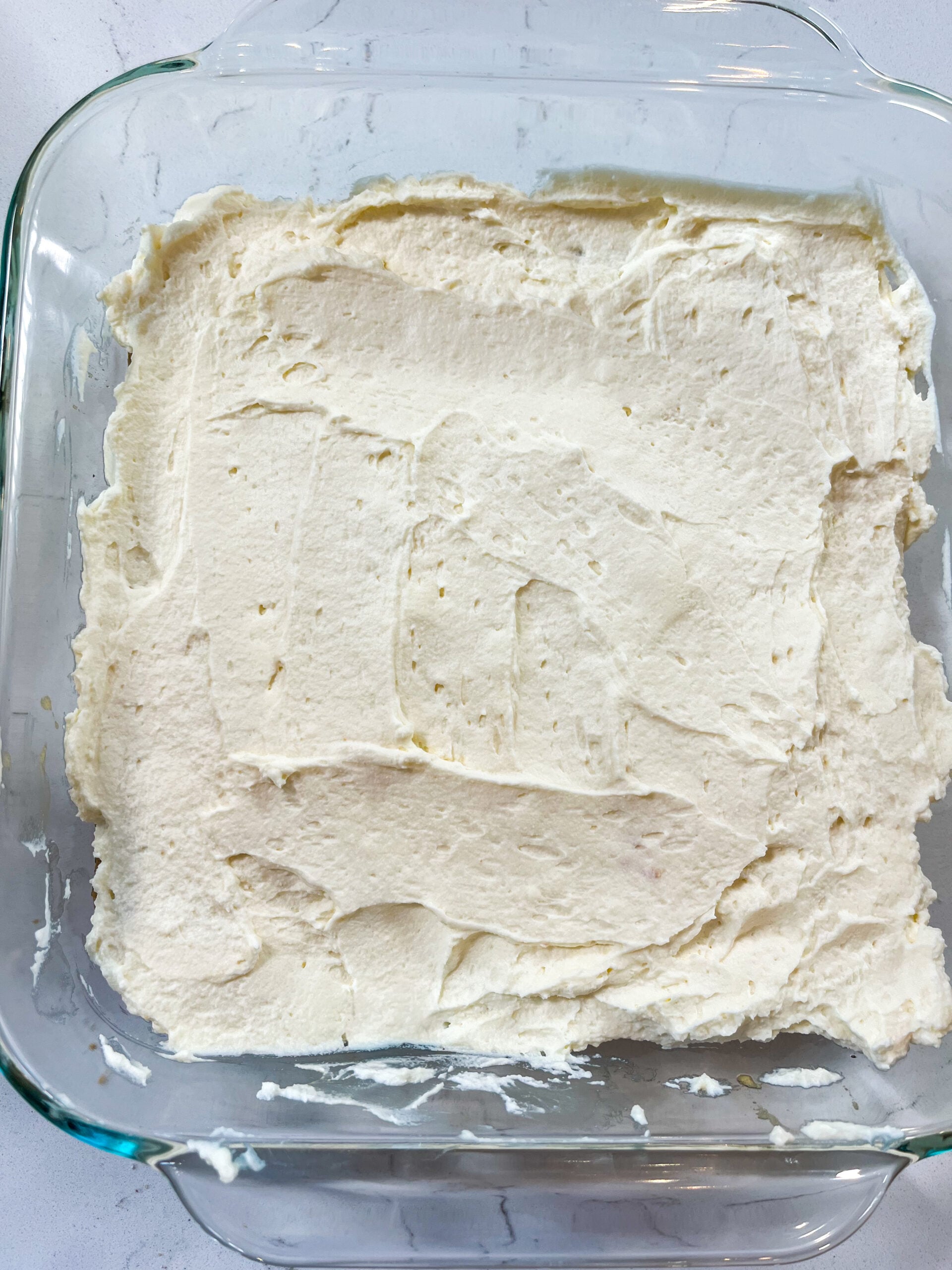 Mascarpone cream mixture spread of ladyfingers in glass baking pan