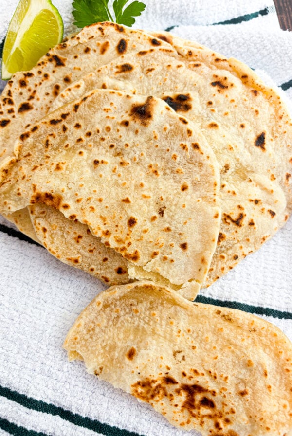 Flour tortillas stacked with one torn on a dish towel