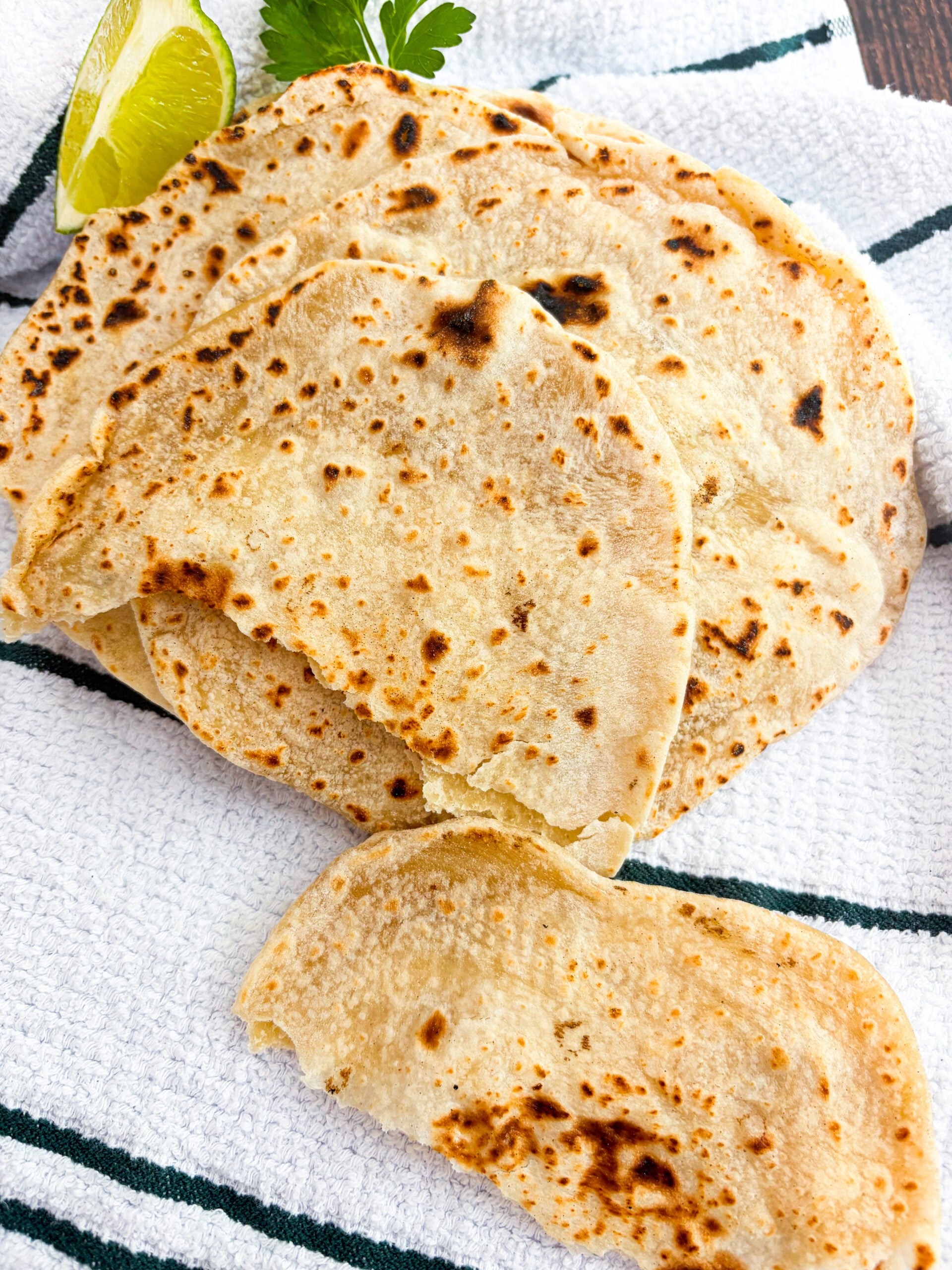 Flour tortillas stacked with one torn on a dish towel
