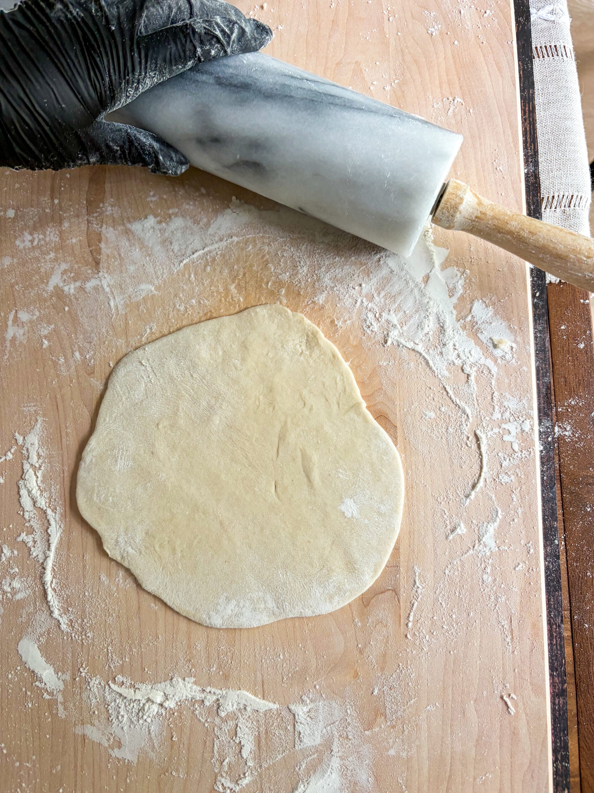 Dough rolled out into tortillas with rolling pin on floured cutting board