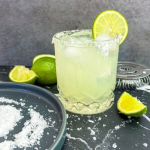Margarita next to salt on plate and lime wedges