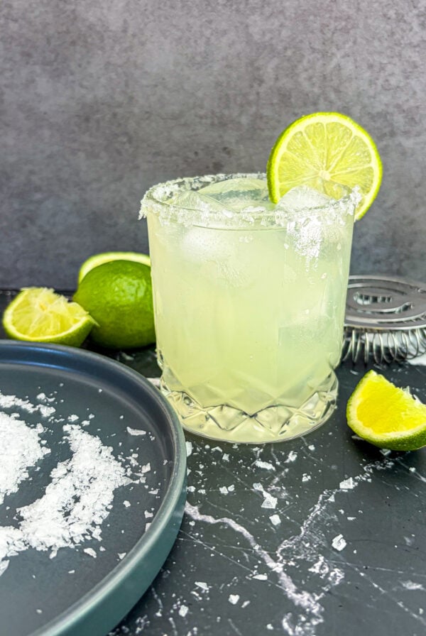 Margarita next to salt on plate and lime wedges