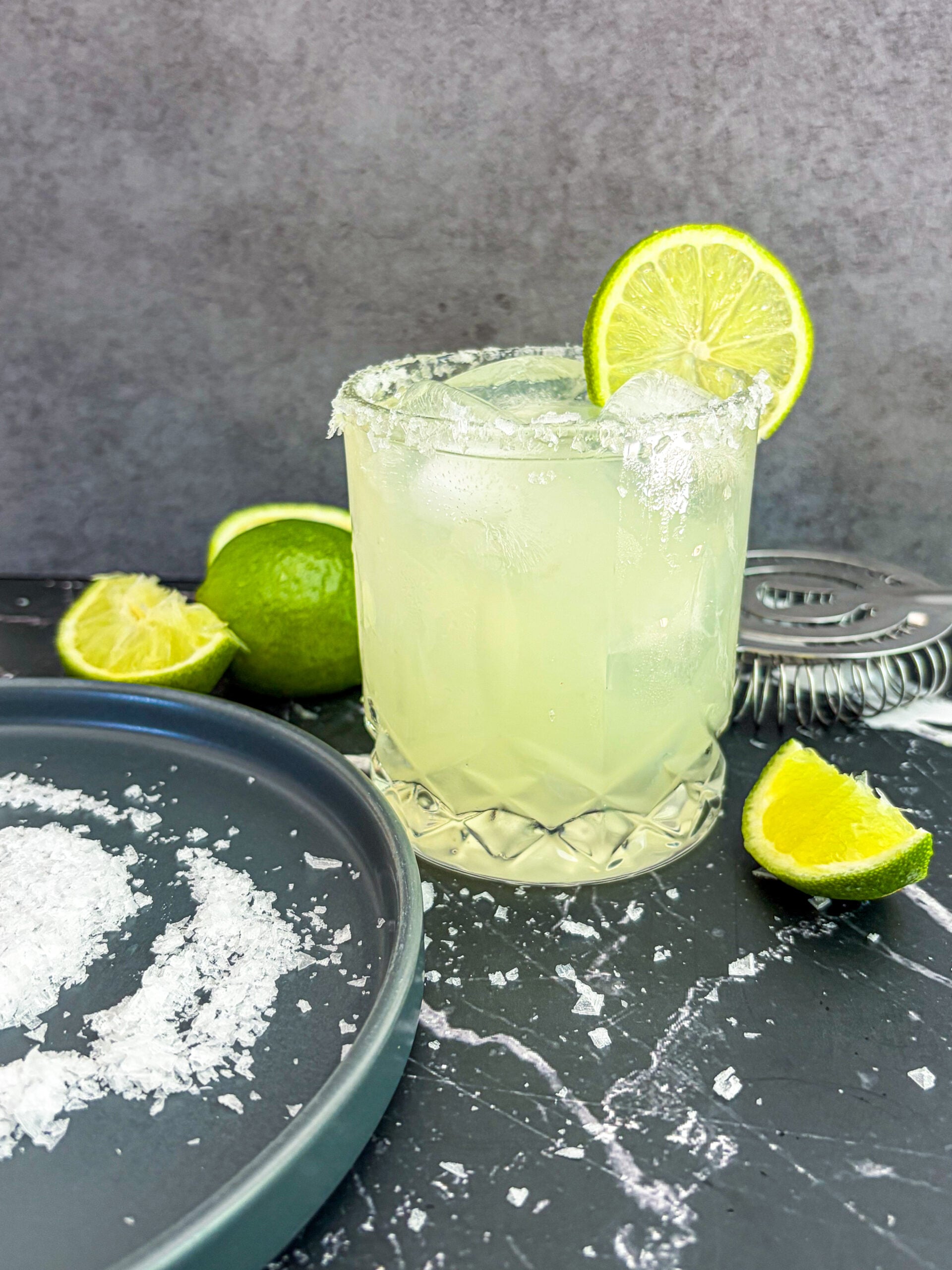 Margarita next to salt on plate and lime wedges