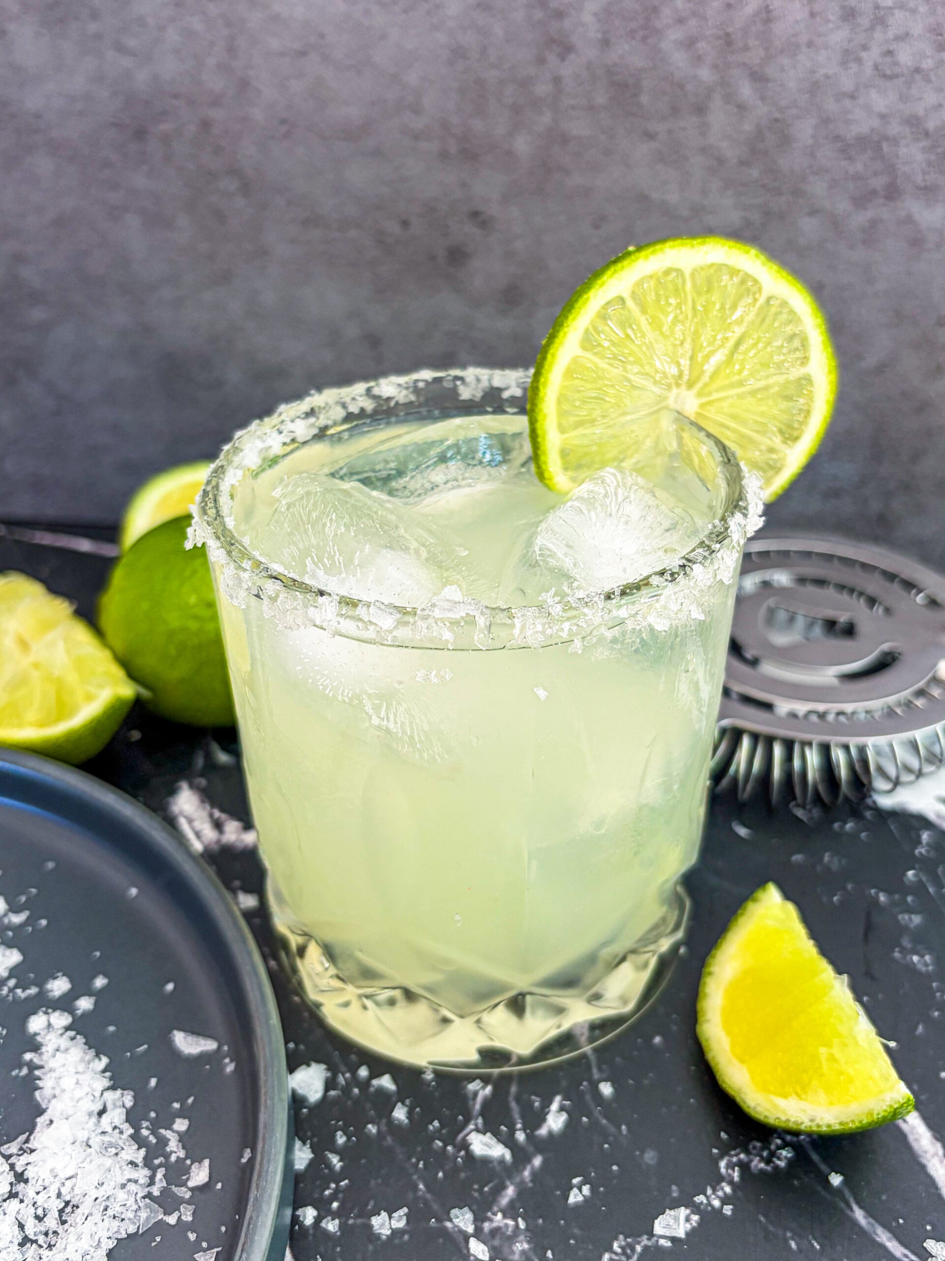 Close up of margarita next to lime wedges and salt on plate