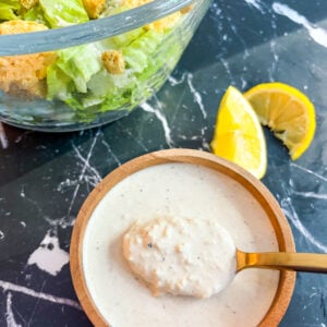 Caesar dressing in a wooden bowl with a spoon next to a Caesar Salad