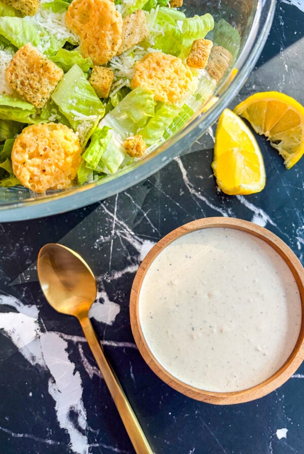 Caesar dressing in a wooden bowl next to a Caesar Salad