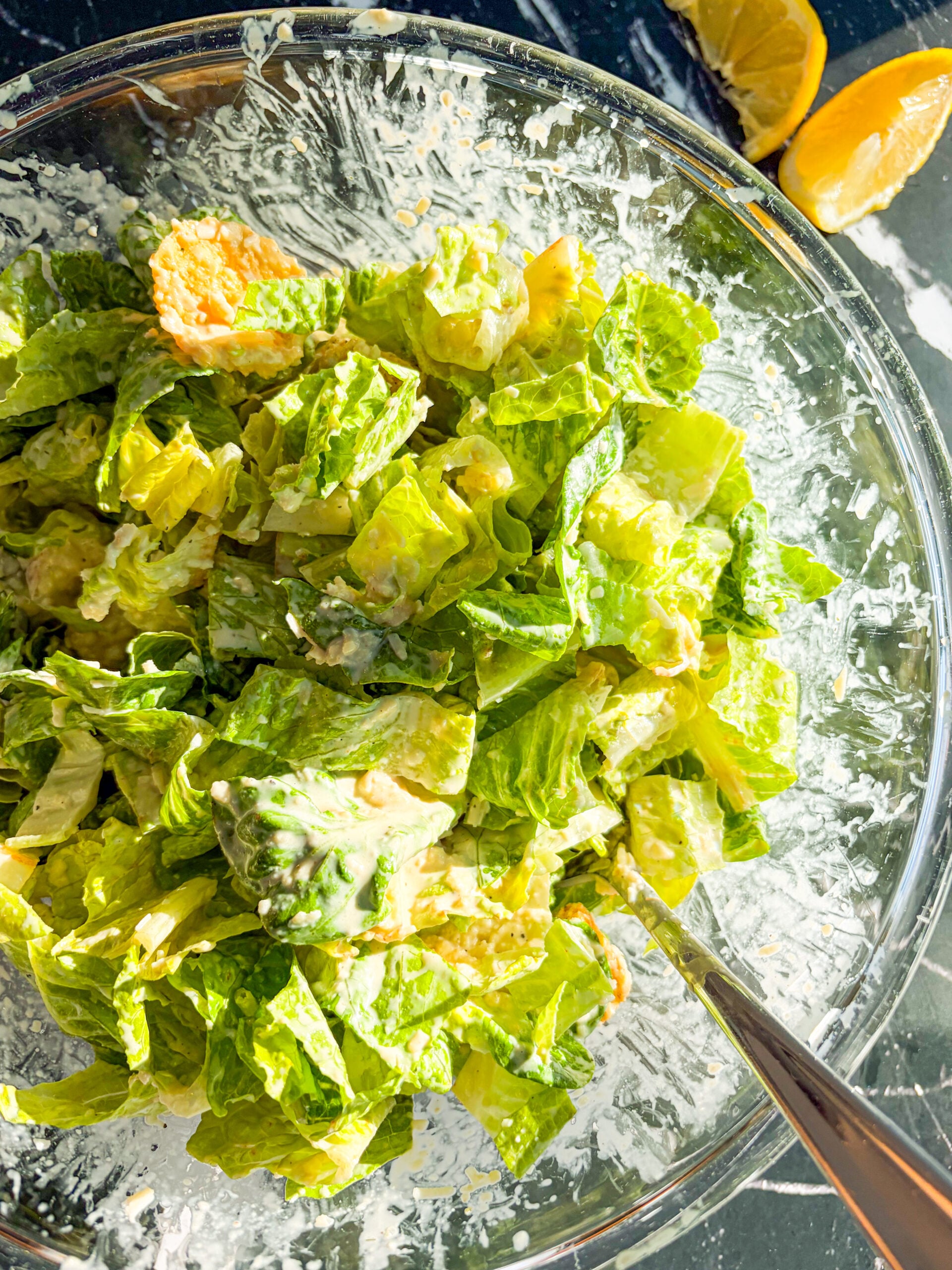 Caesar salad tossed with dressing in a large glass bowl