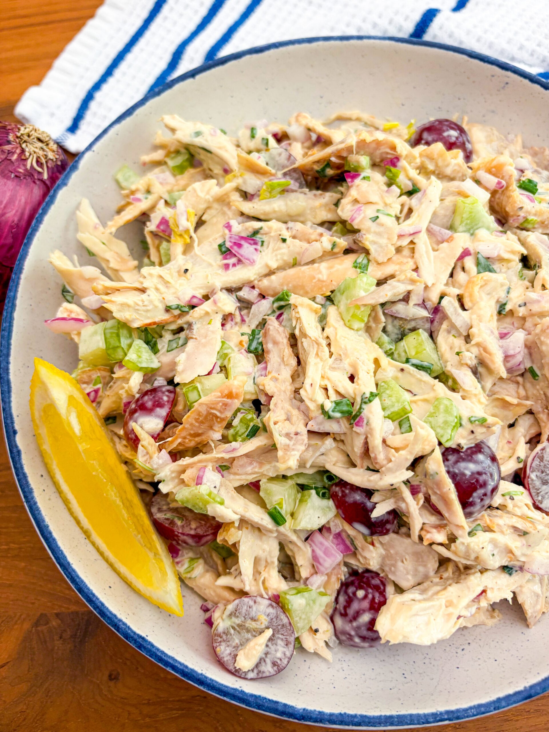 Close up of chicken salad in a blue and white bowl garnished with lemon wedge