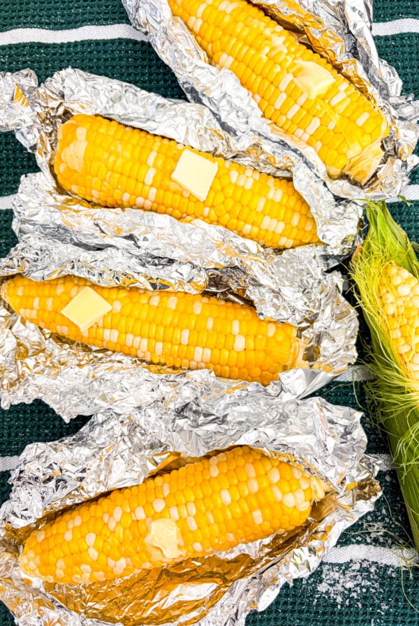 Closer up shot of corn on the cob in foil packages with butter and salt