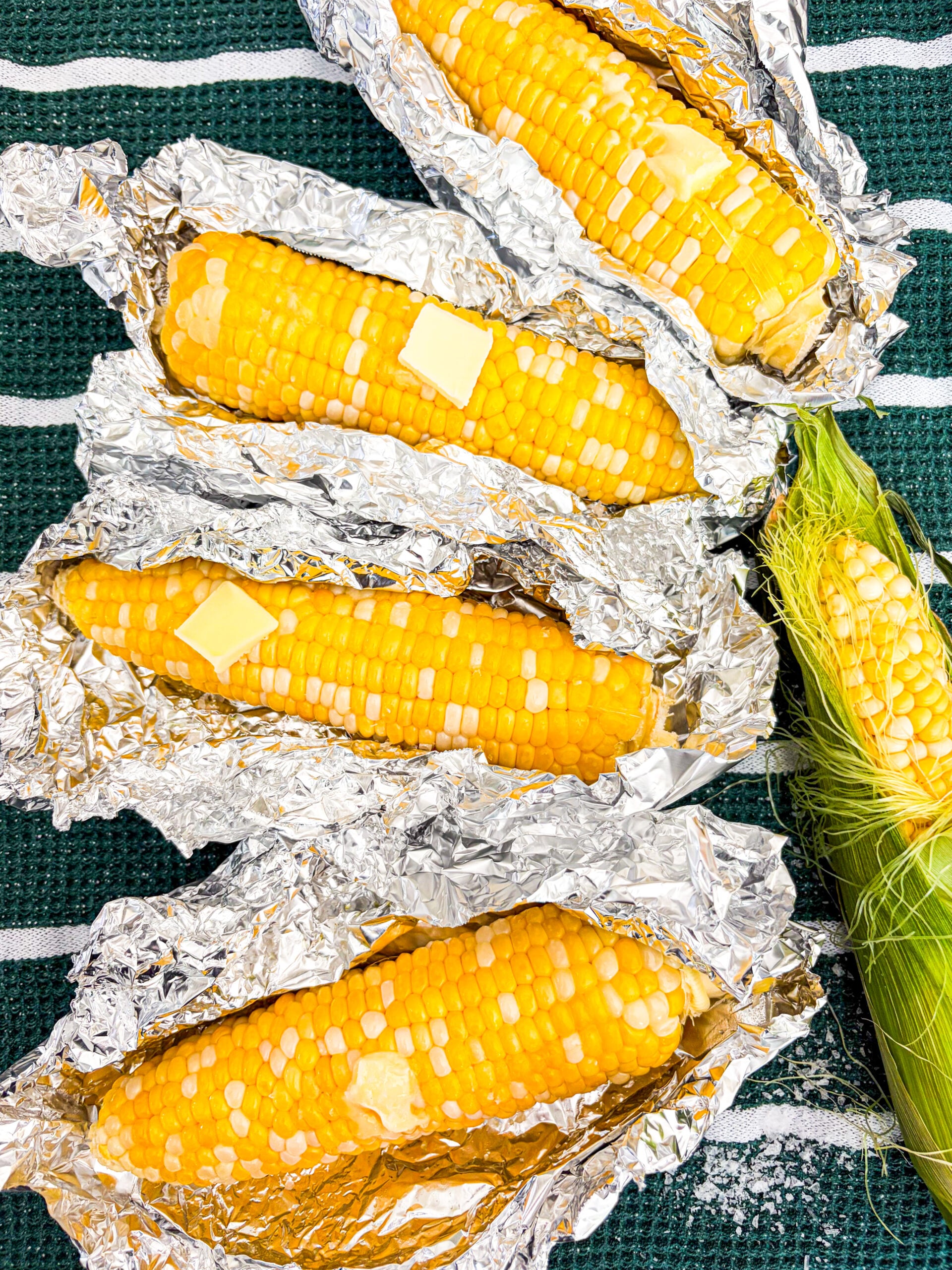 Closer up shot of corn on the cob in foil packages with butter and salt
